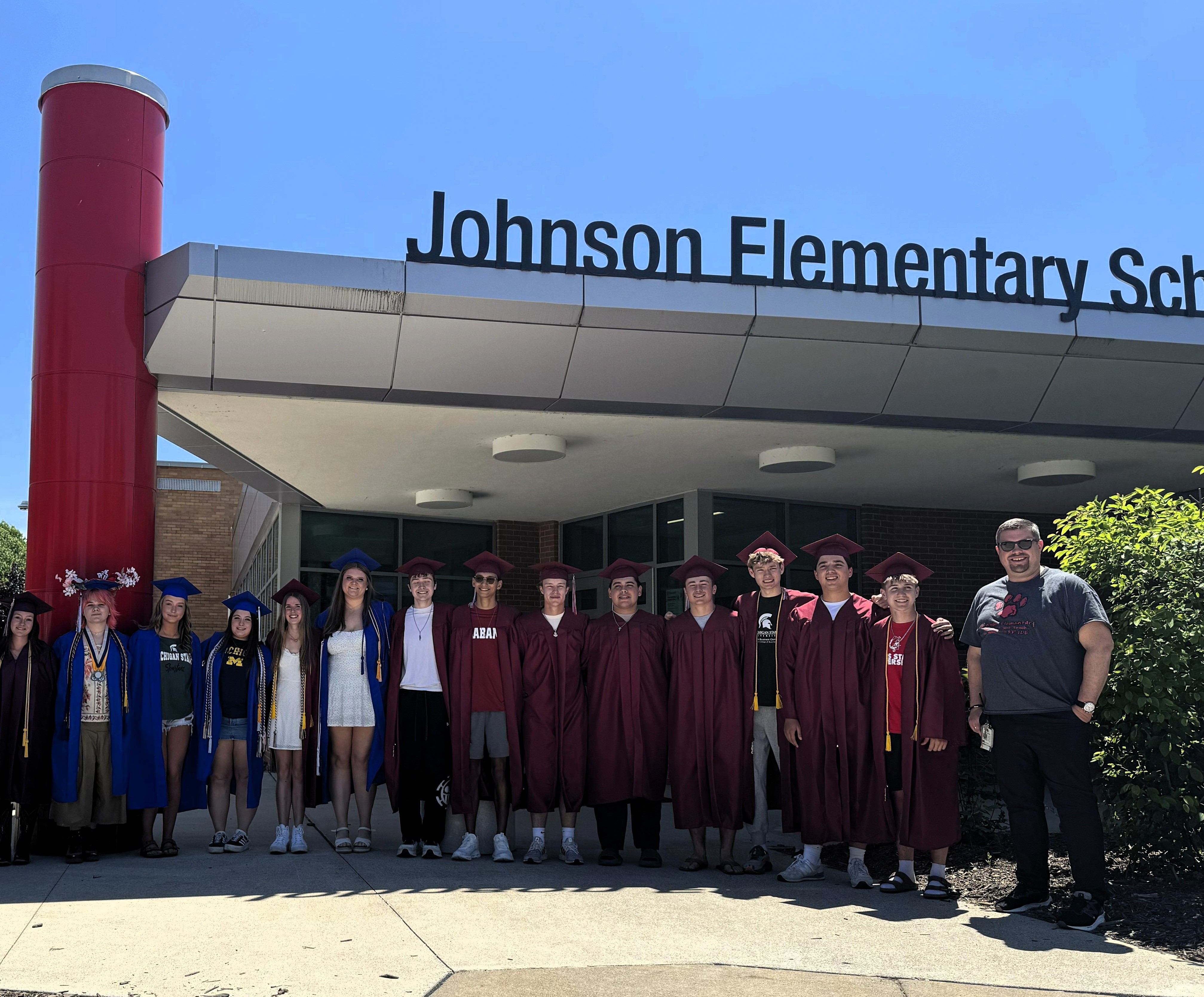 Students in cap & gowns standing and posing for a photo outside a school 