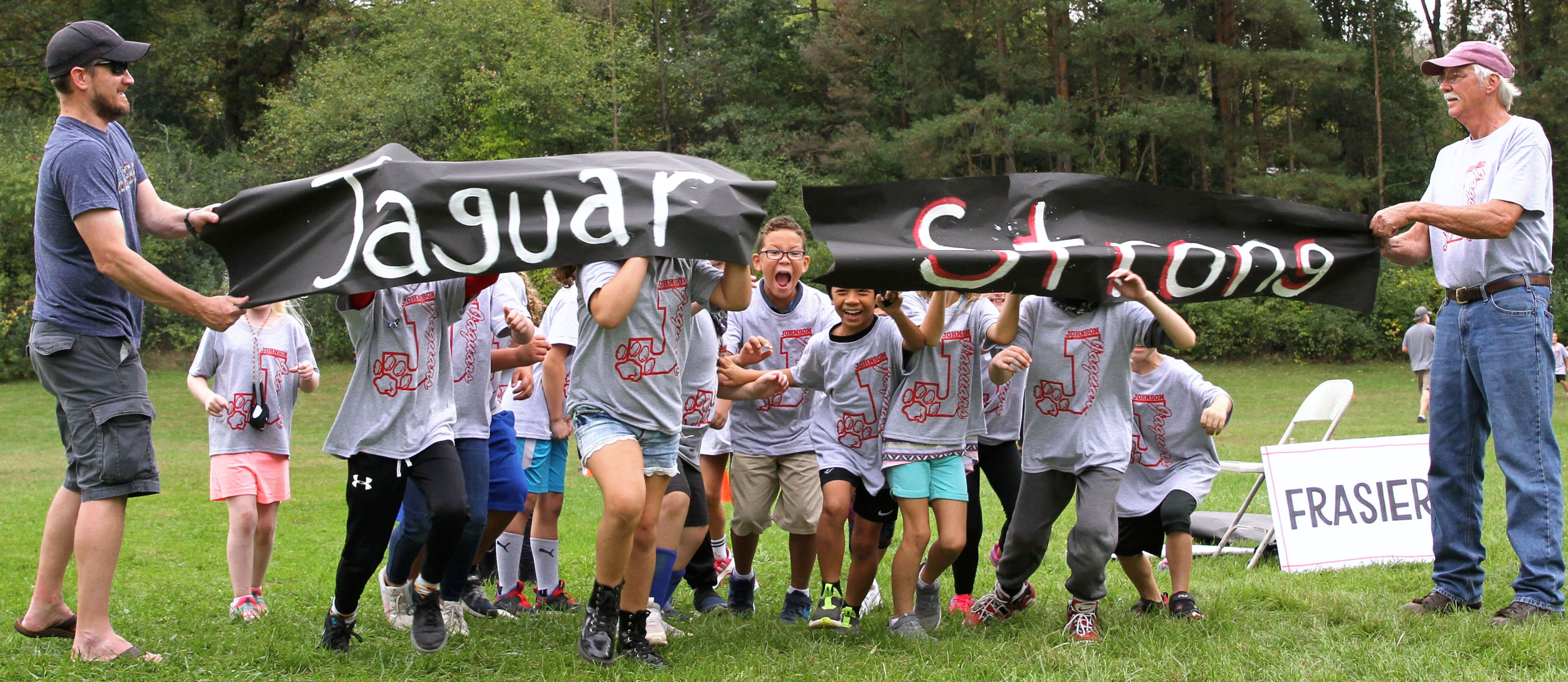 children and adults holding paper sign that says "jaguar strong" for fun run