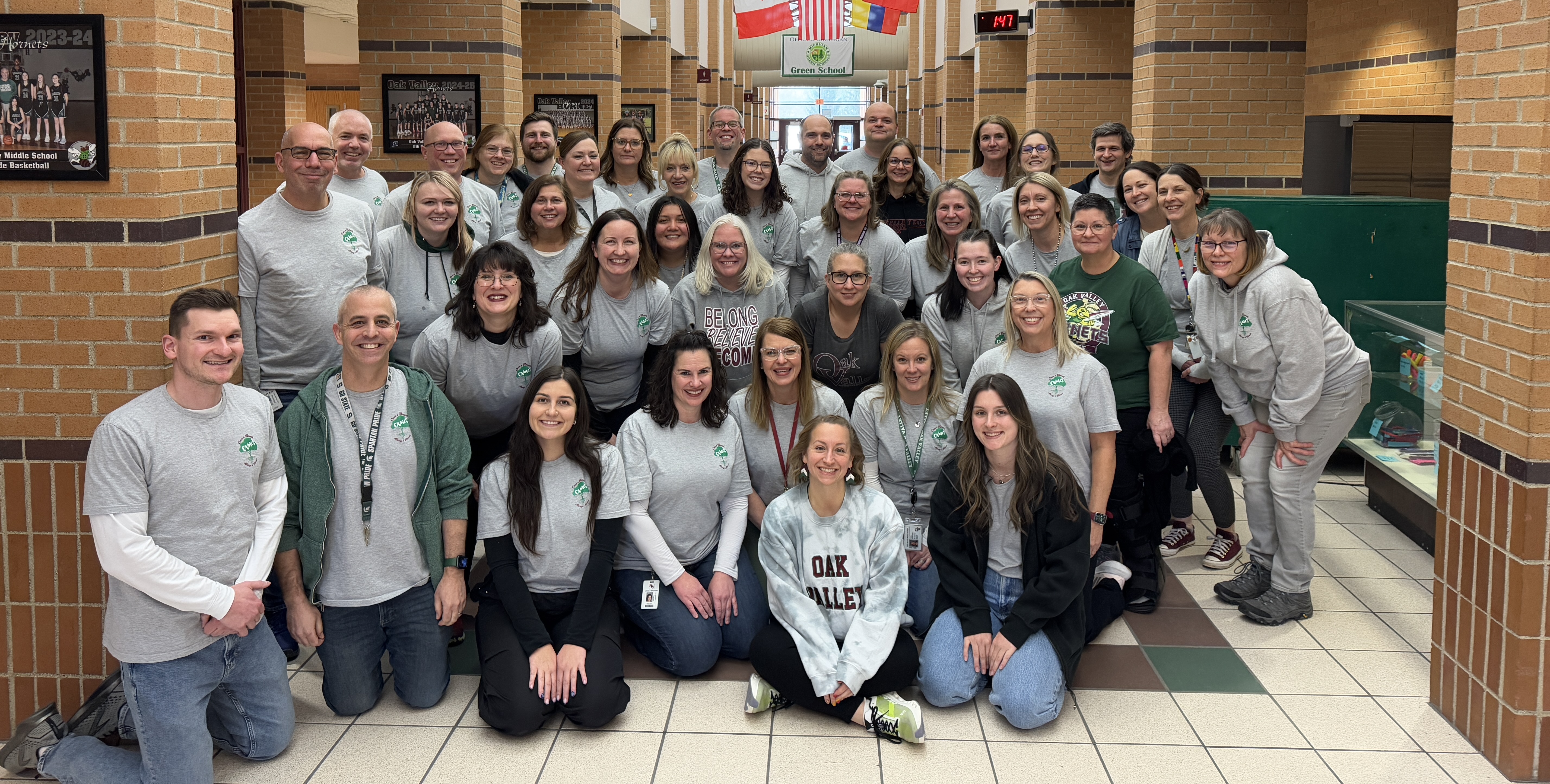 Oak Valley staff standing in hallway underneath flags, all matching in 2025 Oak Valley spirit wear