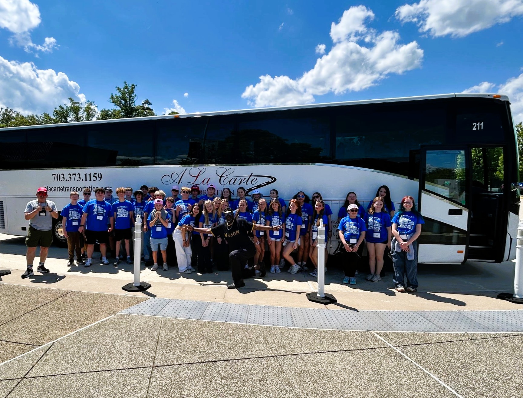 students pose for photo in front of large bus