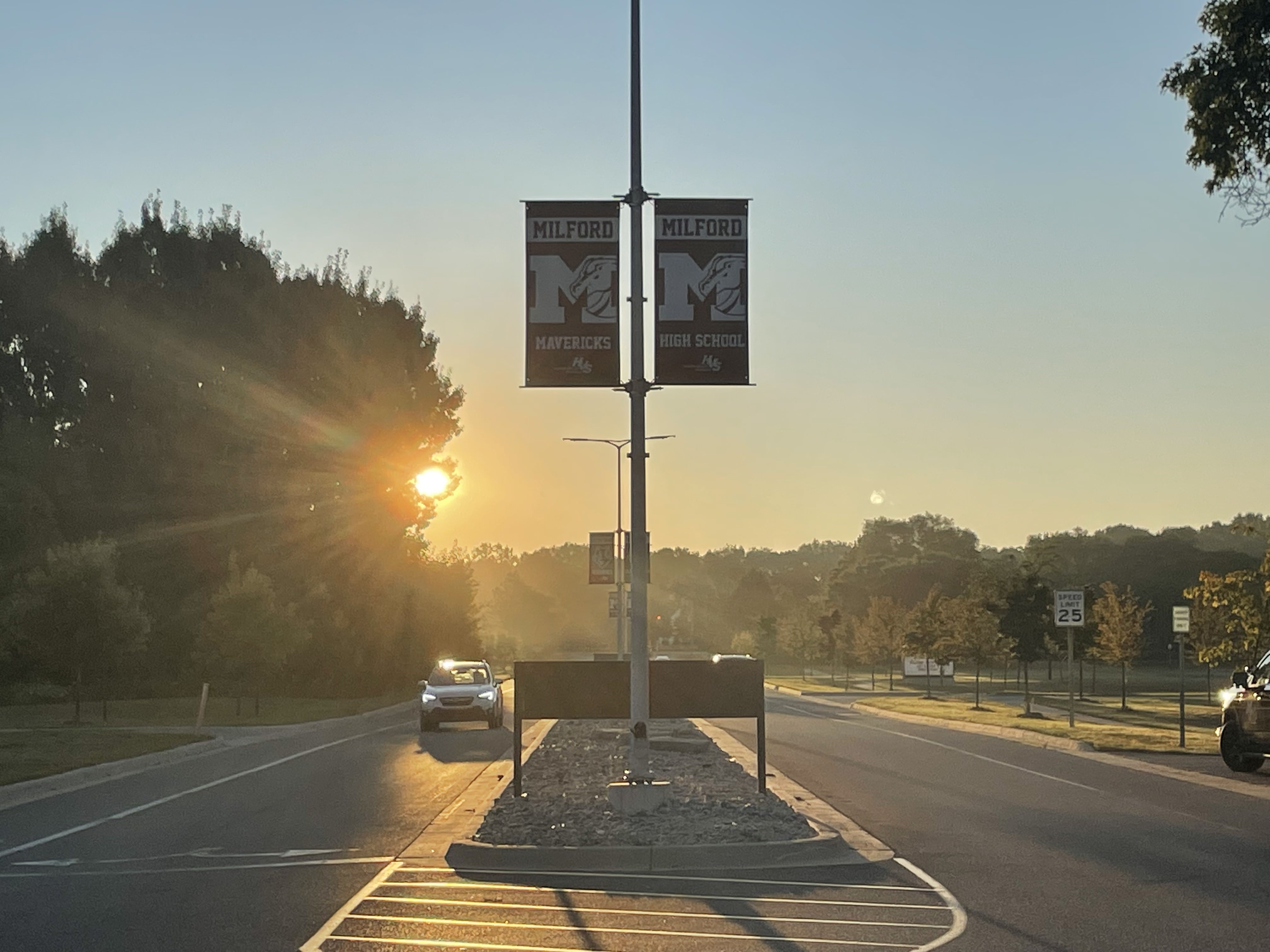 Photo of sunrise down a road with MHS flags on poles