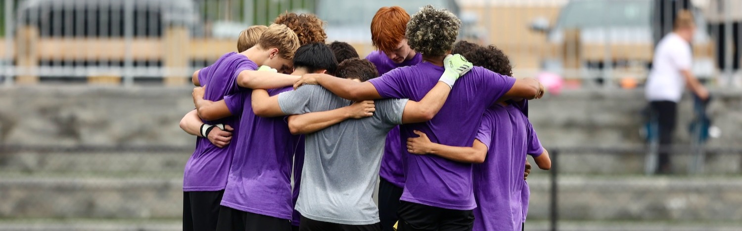 A group of people in purple jerseys and black shorts huddle together on a field.
