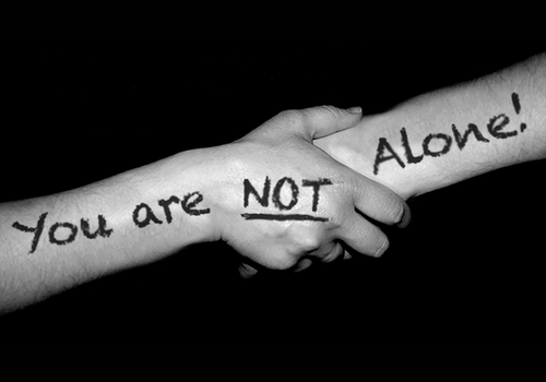 two different hands holding on with "you are not alone" written across their hands/arms