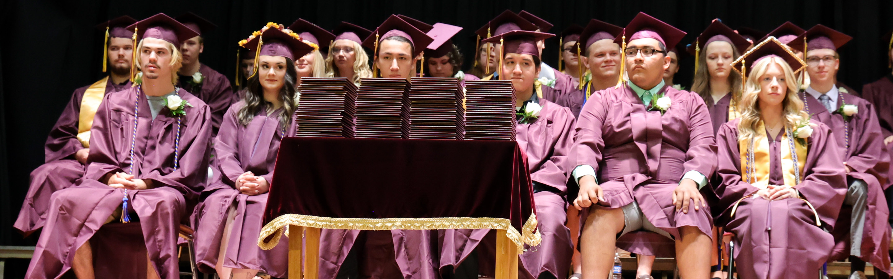 seniors sit on the stage in their caps and gowns at graduation