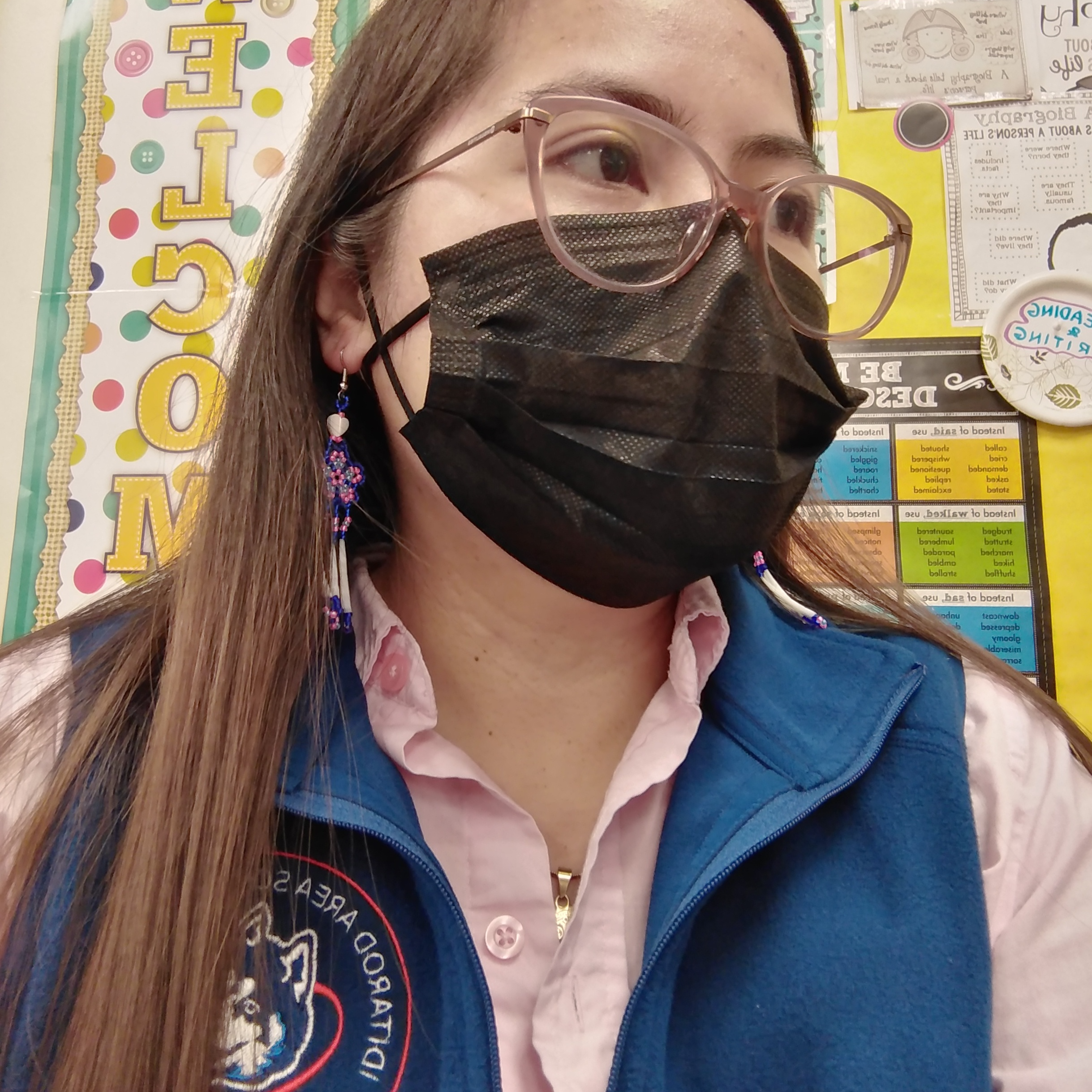 Image of Jollibe in classroom wearing blue iditarod vest with black facemask and glasses
