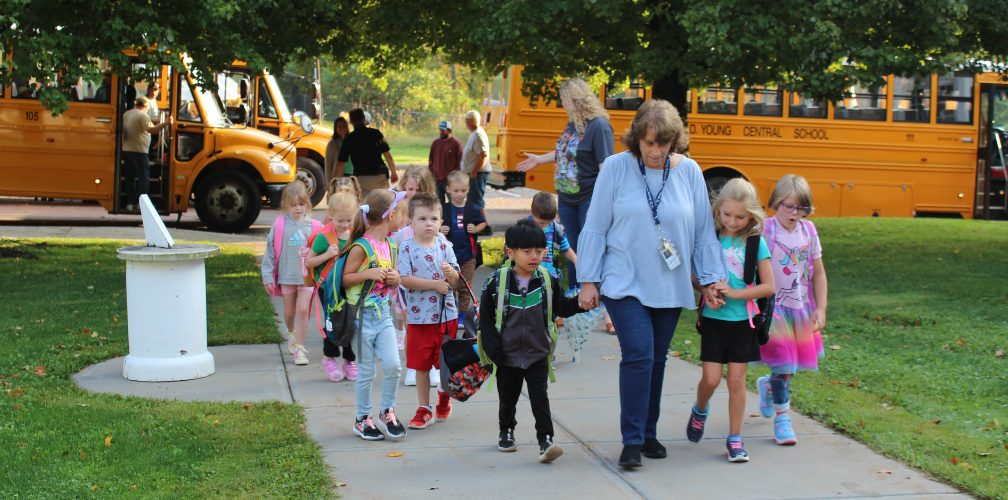 a teacher leads young students down a sidewalk