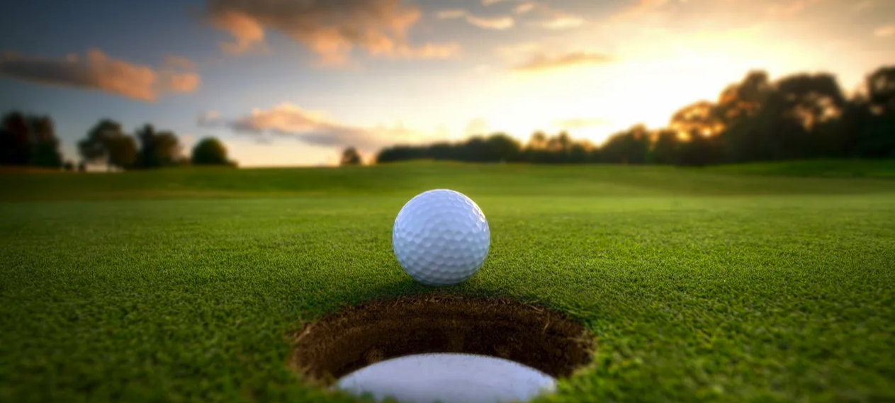 Sunset behind a golf ball in front of a hole on the green