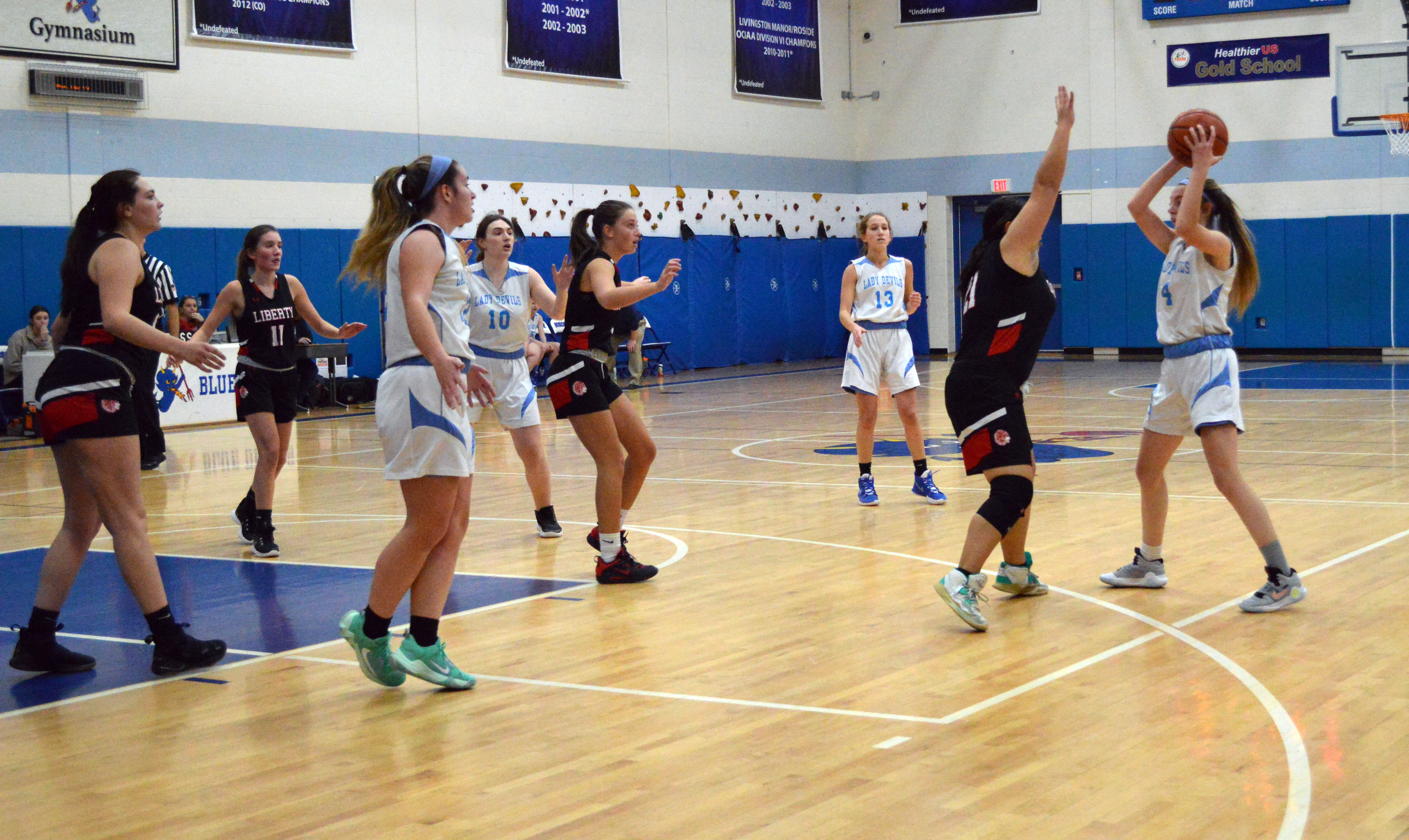 A girl prepares to throw a basketball to her teammates under the basket at the opposing team defends