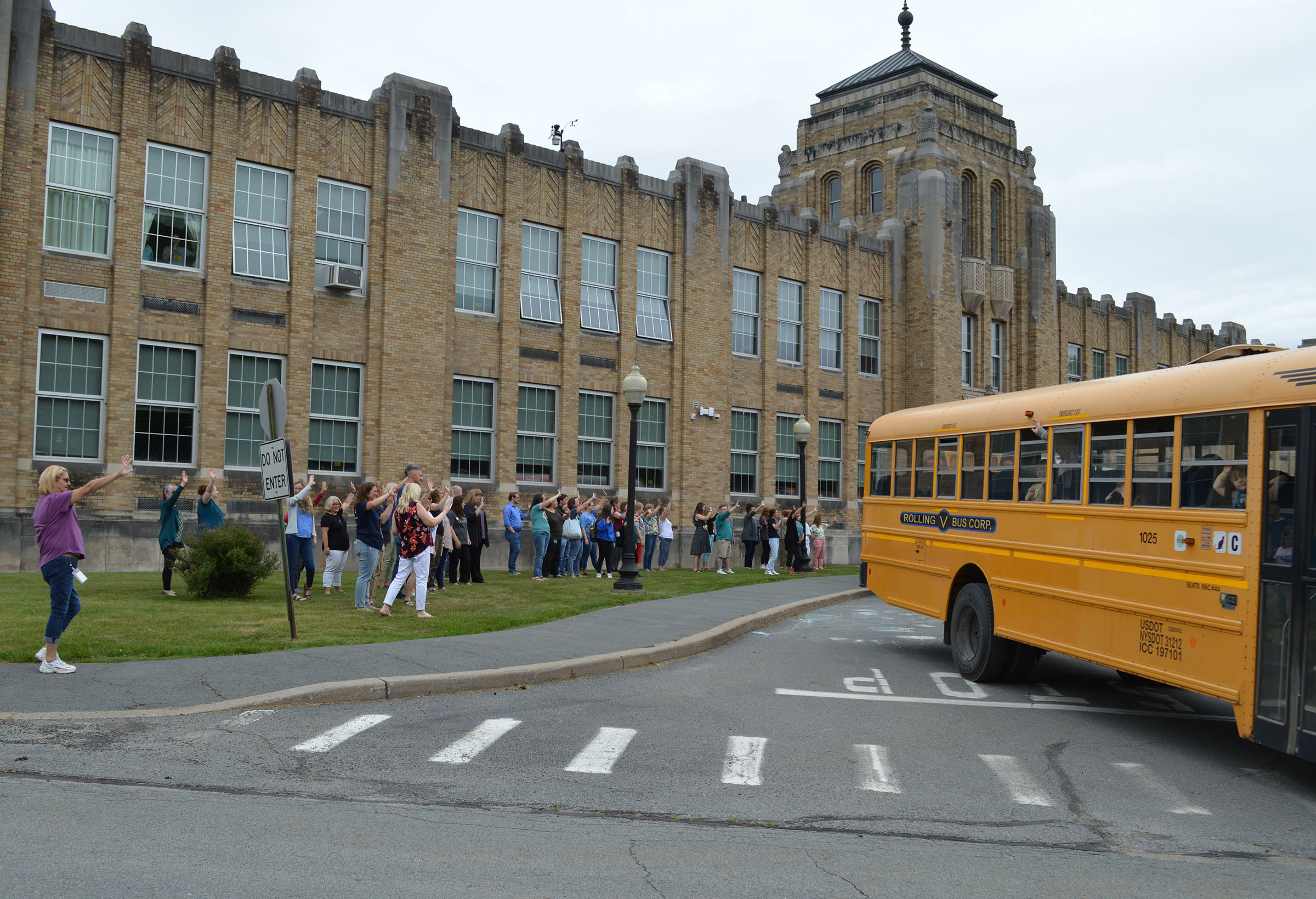 Staff wave to buses as they leave the bus loop in front of the school