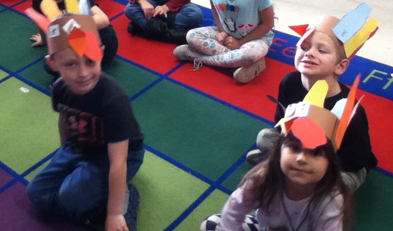 students wearing turkey crowns sit on a carpet