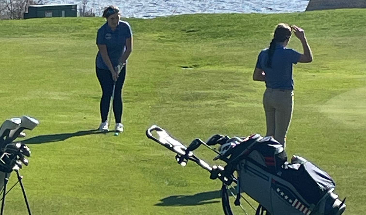 Two students play golf near a body of water