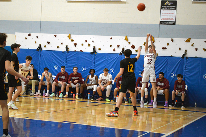 A basketball player makes a shot as his teammates on the bench watch behind him and defenders try to block