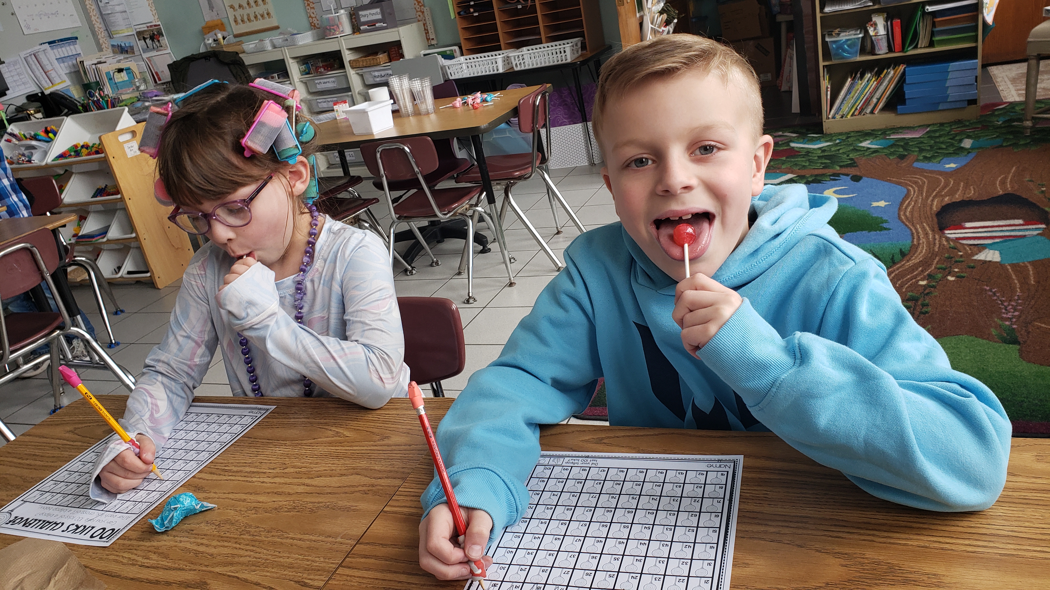 Two students lick lollipops and work on a 100 days of school worksheet