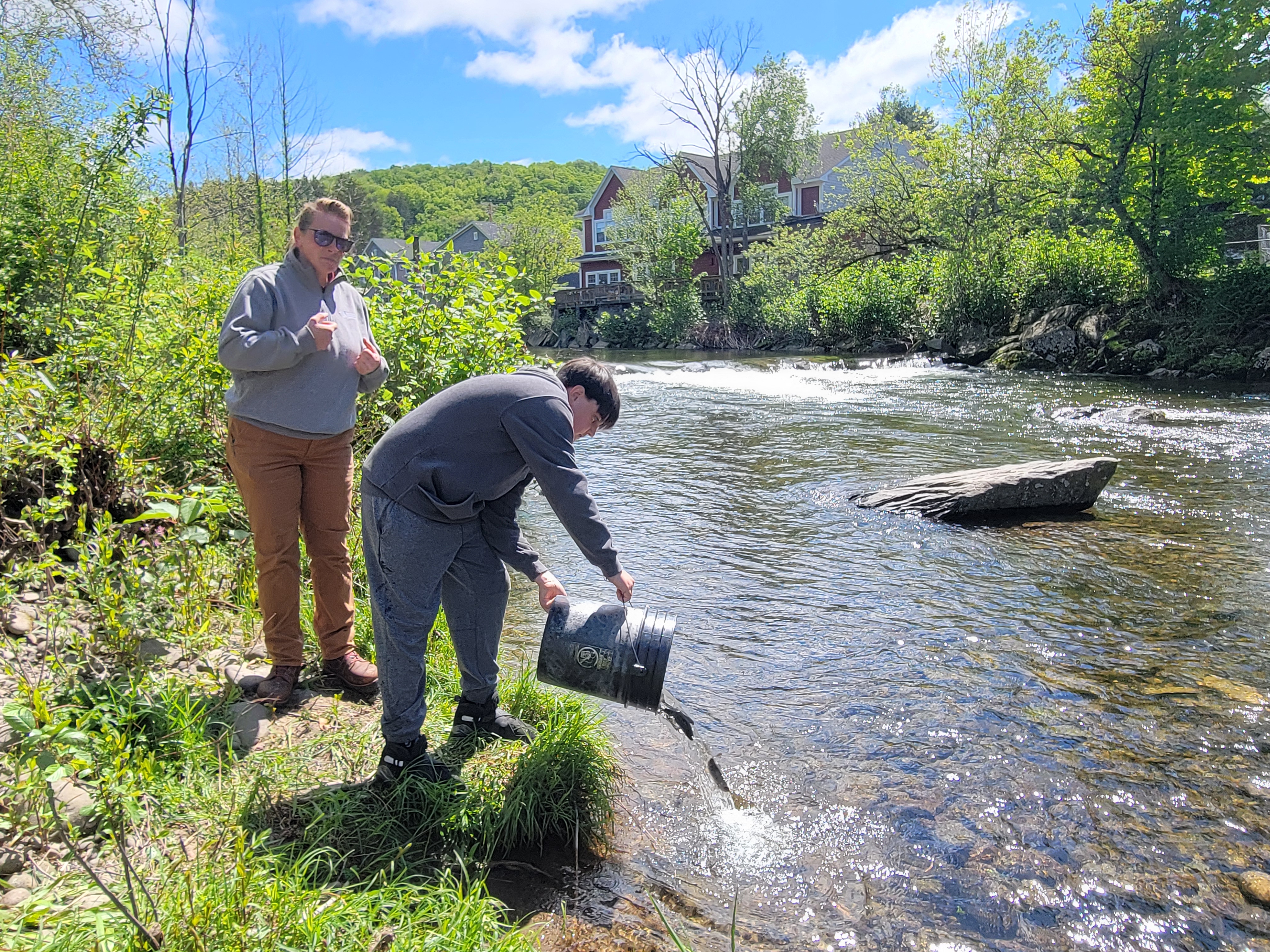 A student dumps fingerling trout into a creek as an adult watches