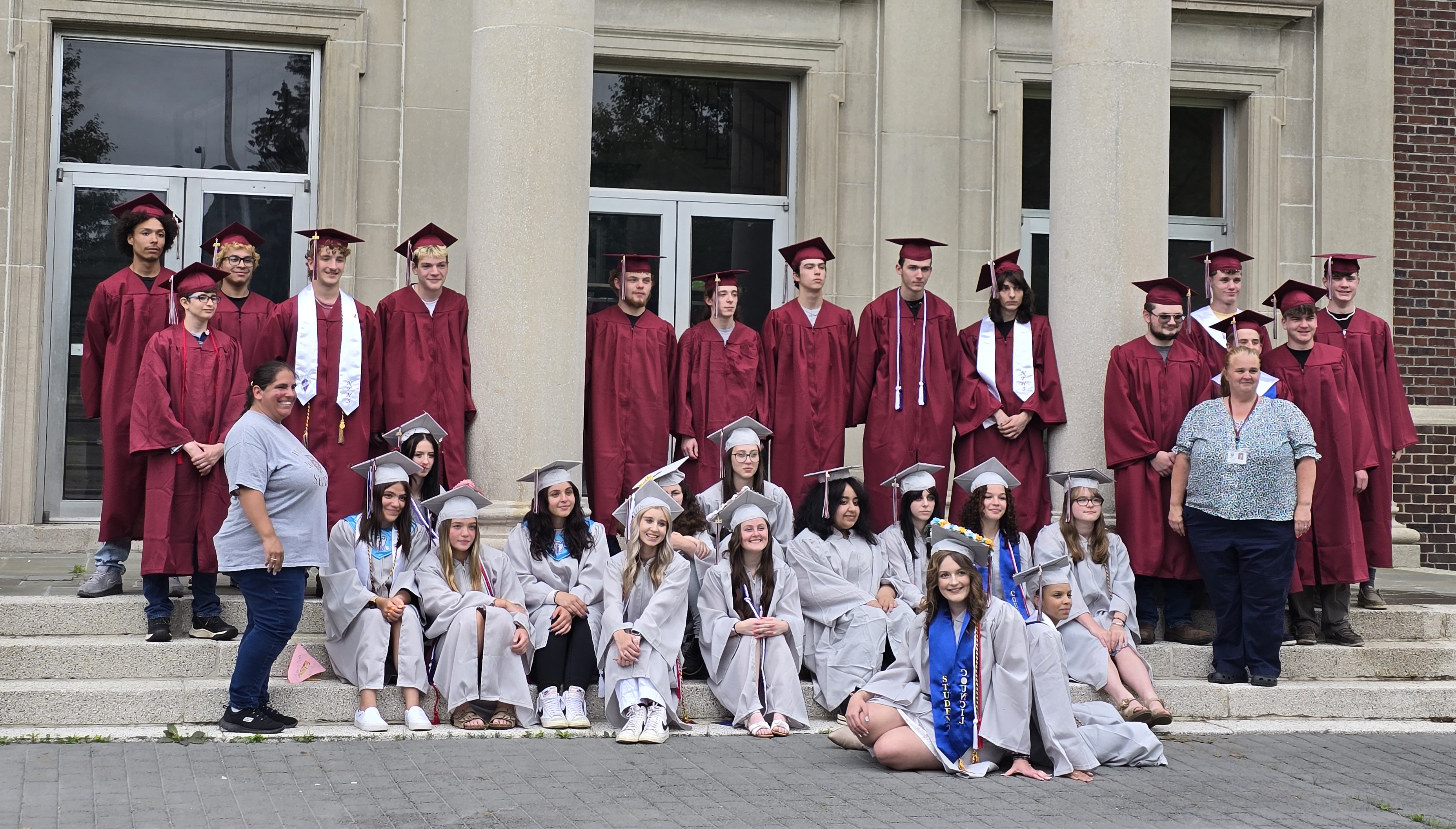 Students in caps and gowns pose in front of the school for photos with their advisors.