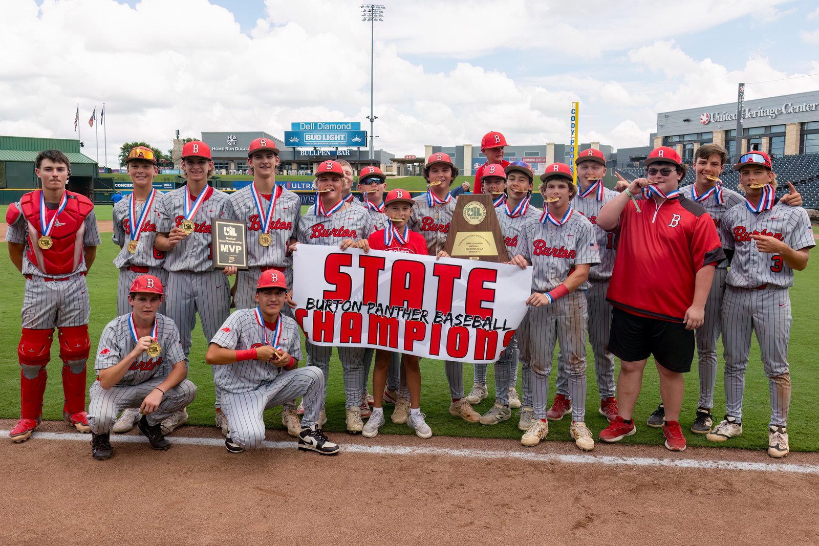 Group of boys dressed in baseball uniforms surrounding a sign that says State Champions