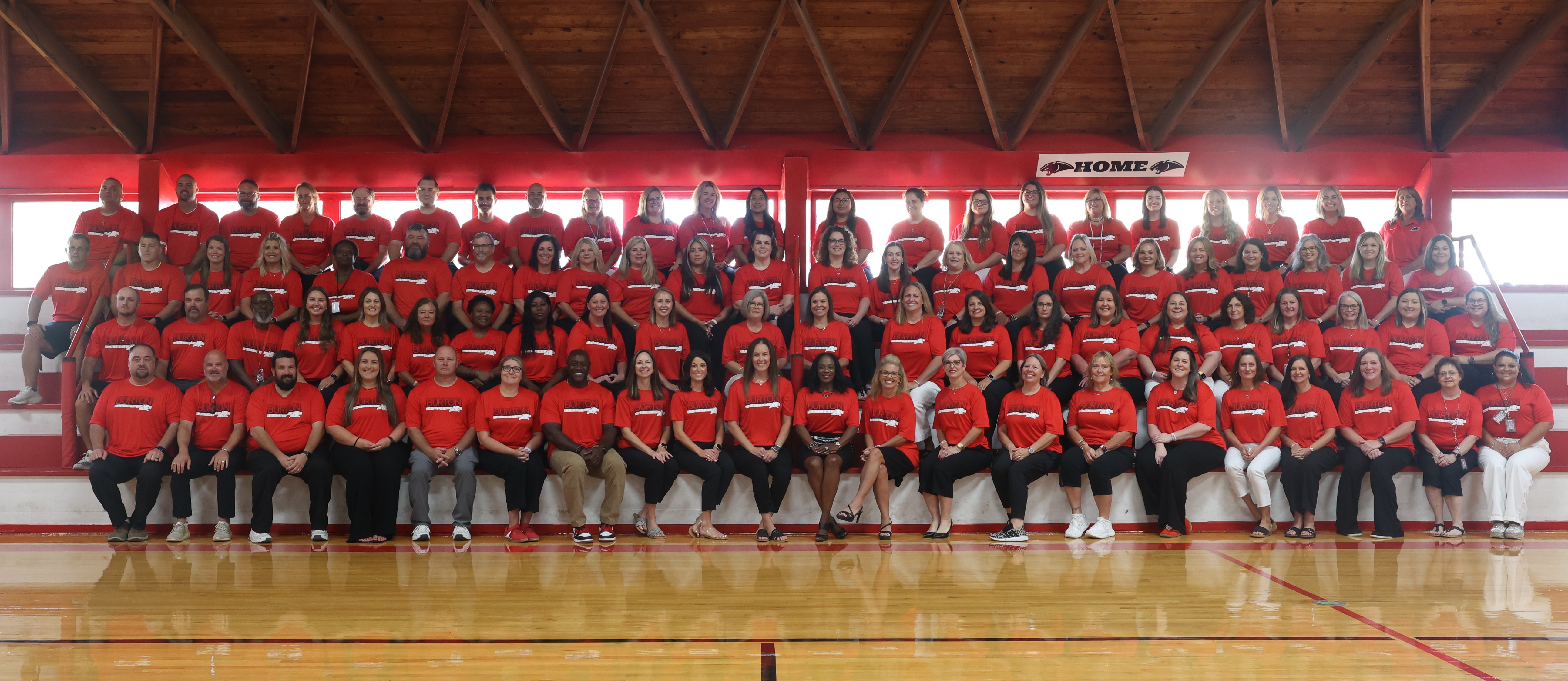 Group of adults in red shirts seated in bleachers smiling at the camera