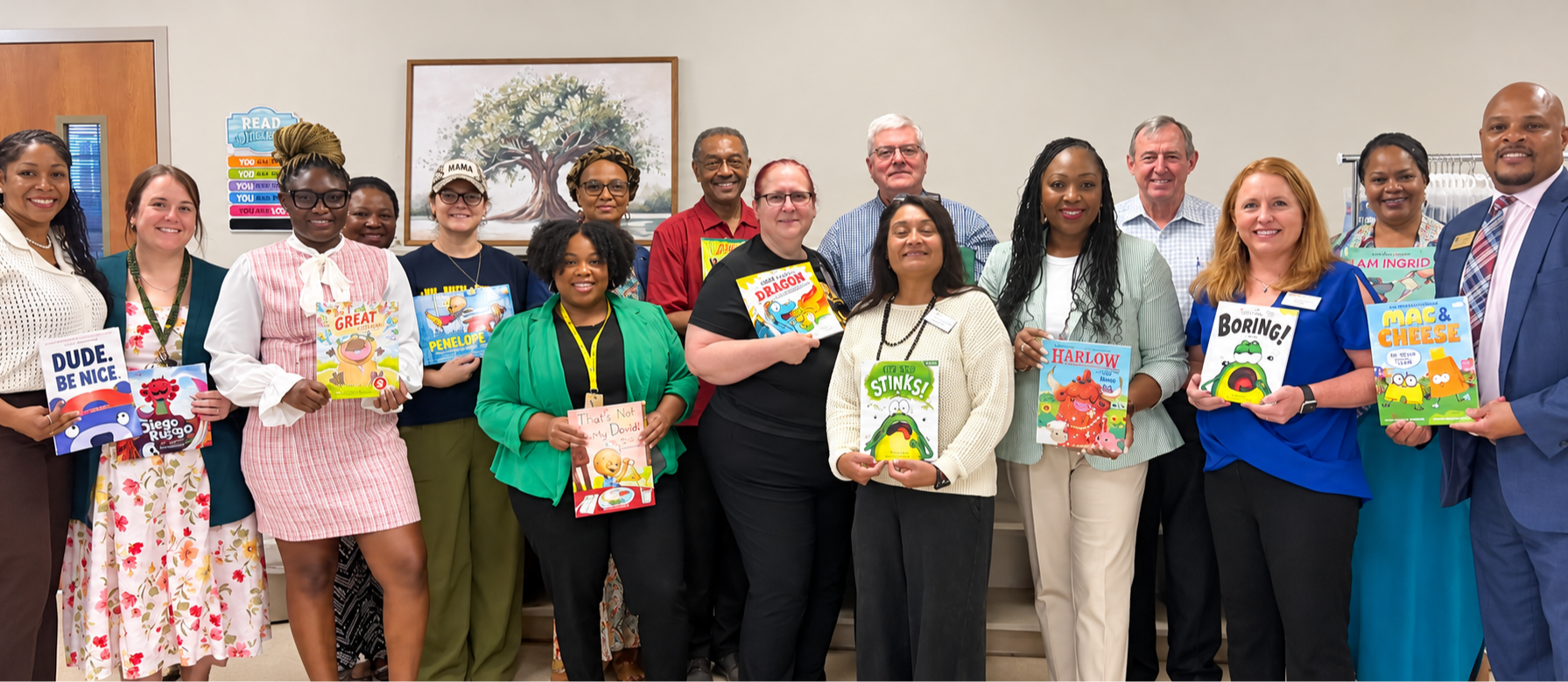 A group of adults pose for a picture indoors, holding books, with a plain background.