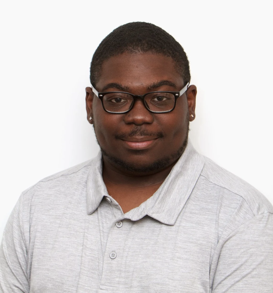 Photo of black male with glasses, diamond earring studs, gray collared shirt