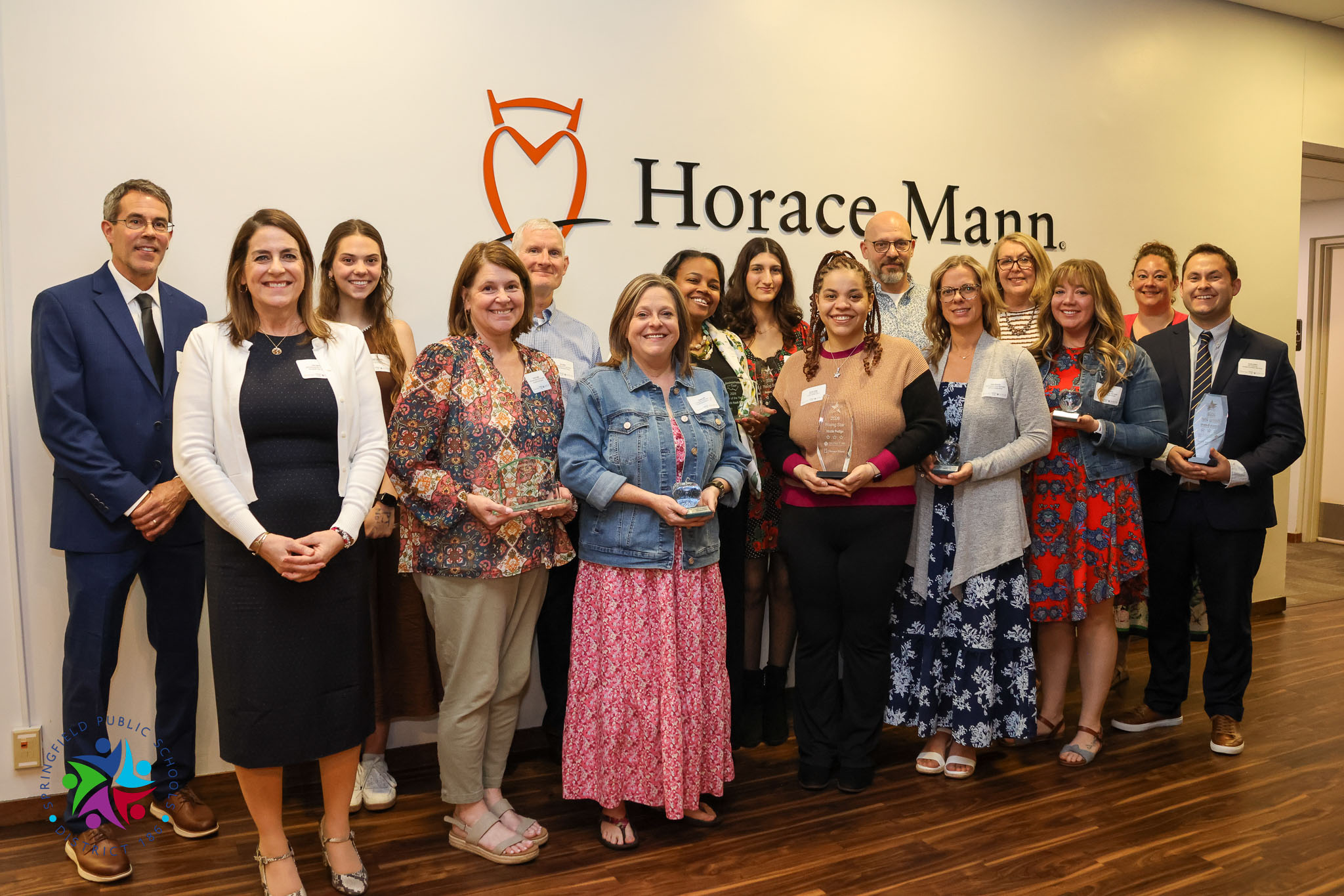 A group of adults posing for a picture. Some are holding awards. They are in front of a Horace Mann sign.