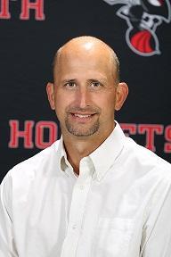 headshot of Russell in front of Hornets backdrop, smiling with no hair, and white button down