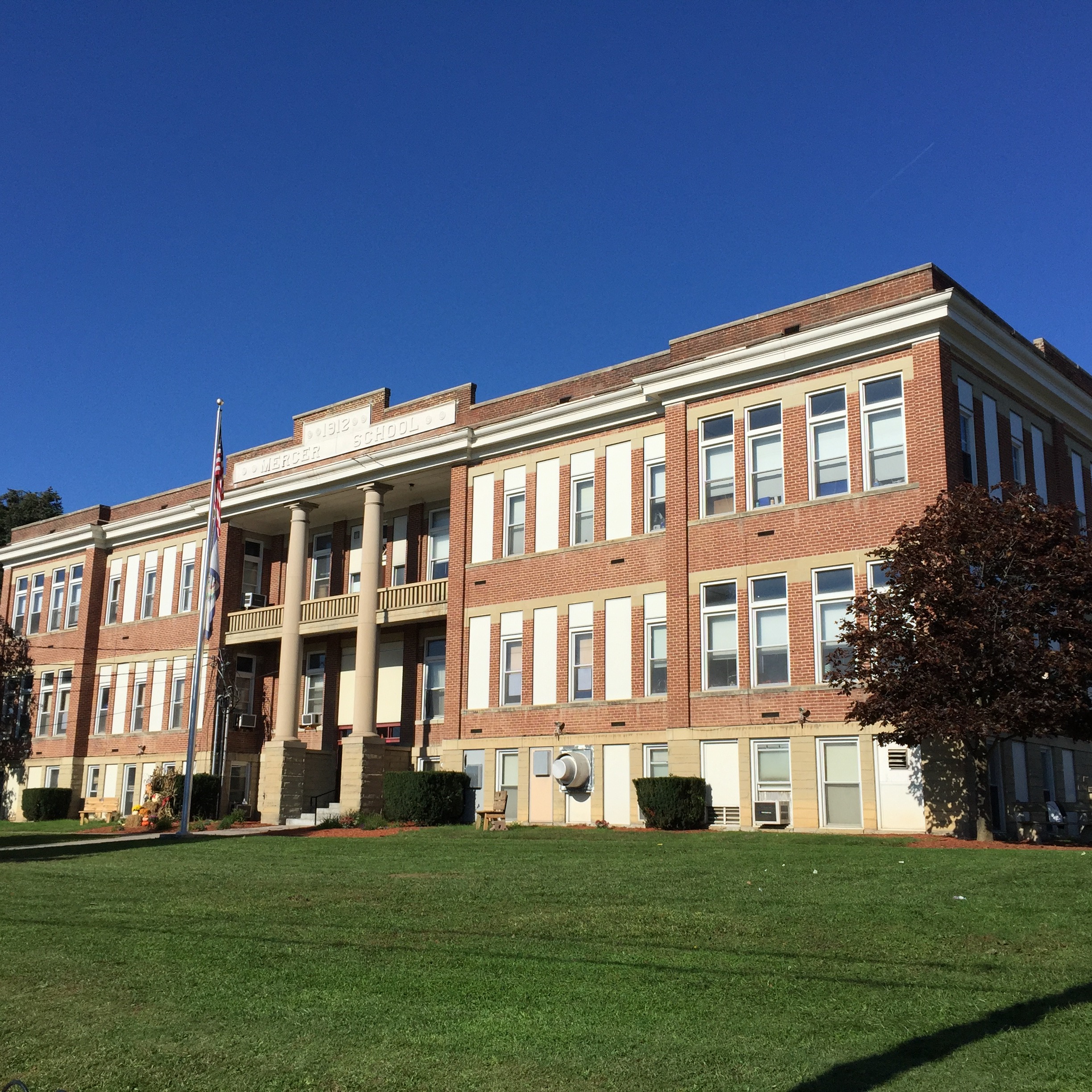 Brick building with many windows and a flagpole in front, set on a grassy lawn.
