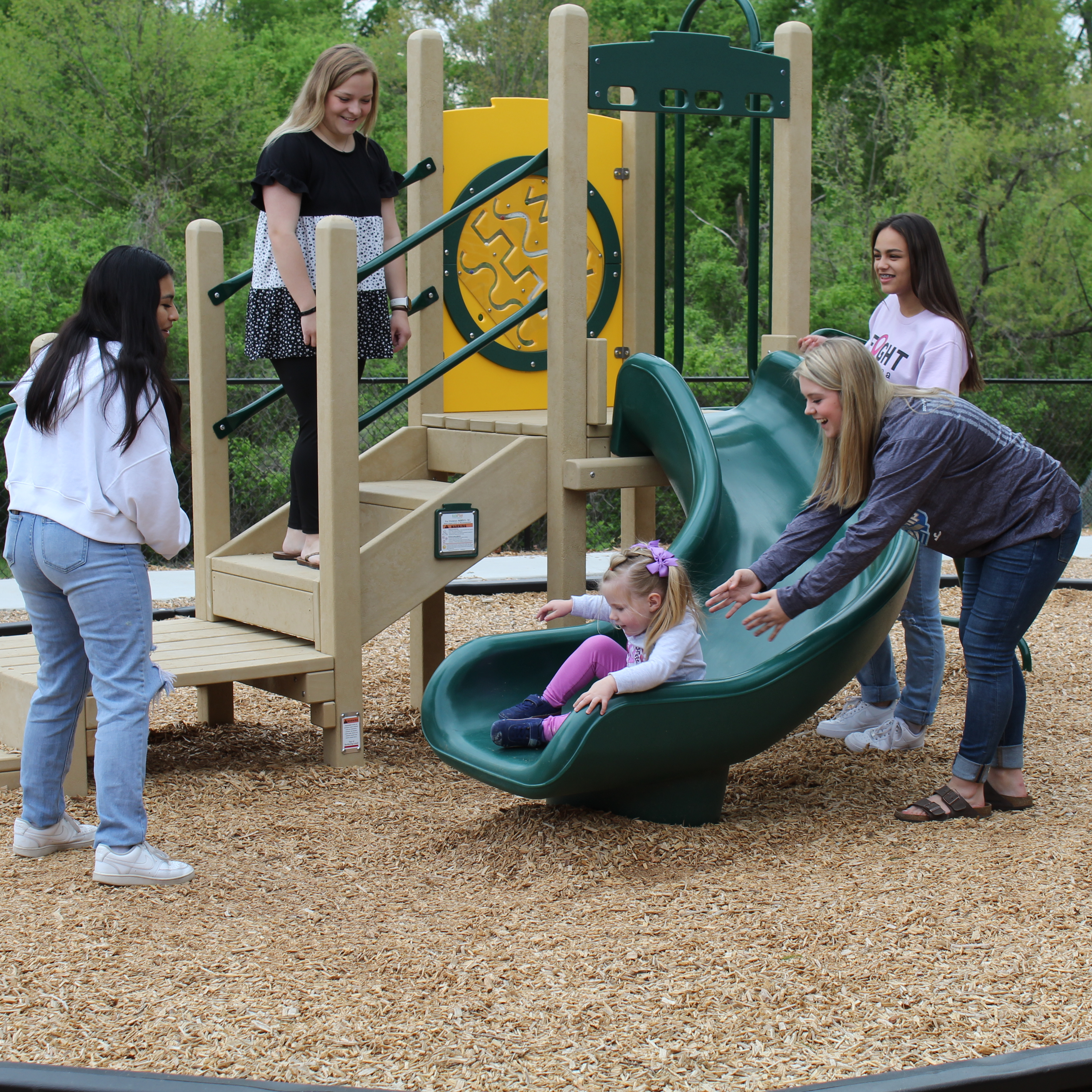 a group of adults play with a toddler on the playground