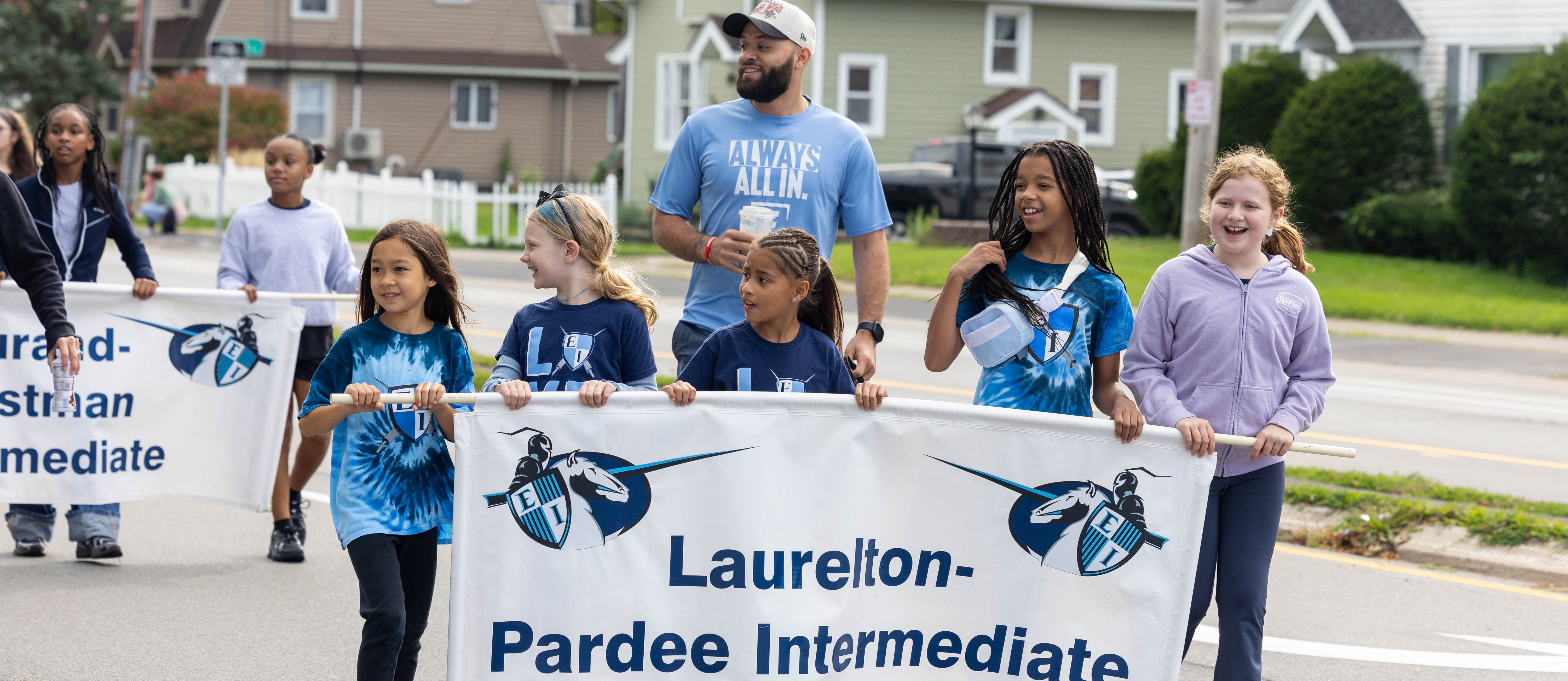students hold up banner with teacher in a parade