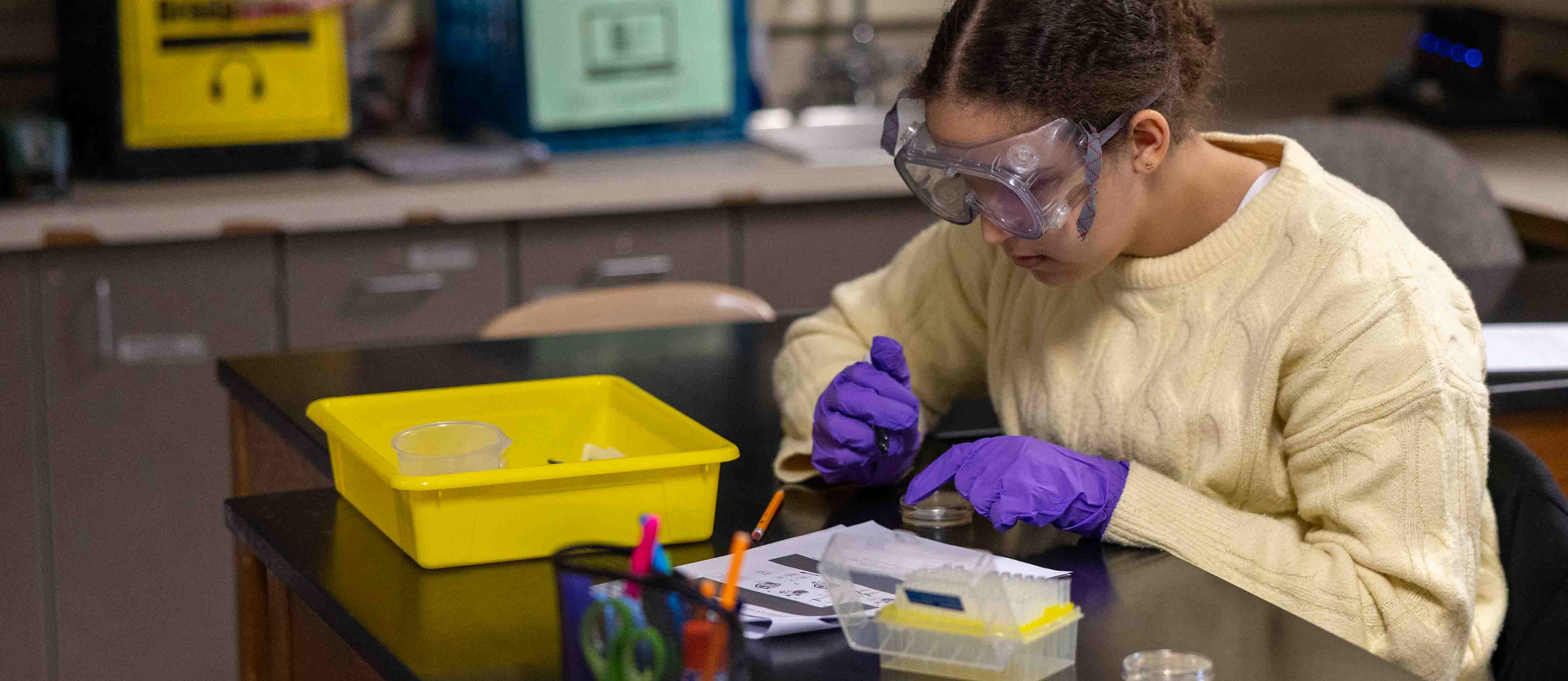 Student works in the science classroom with safety googles and gloves