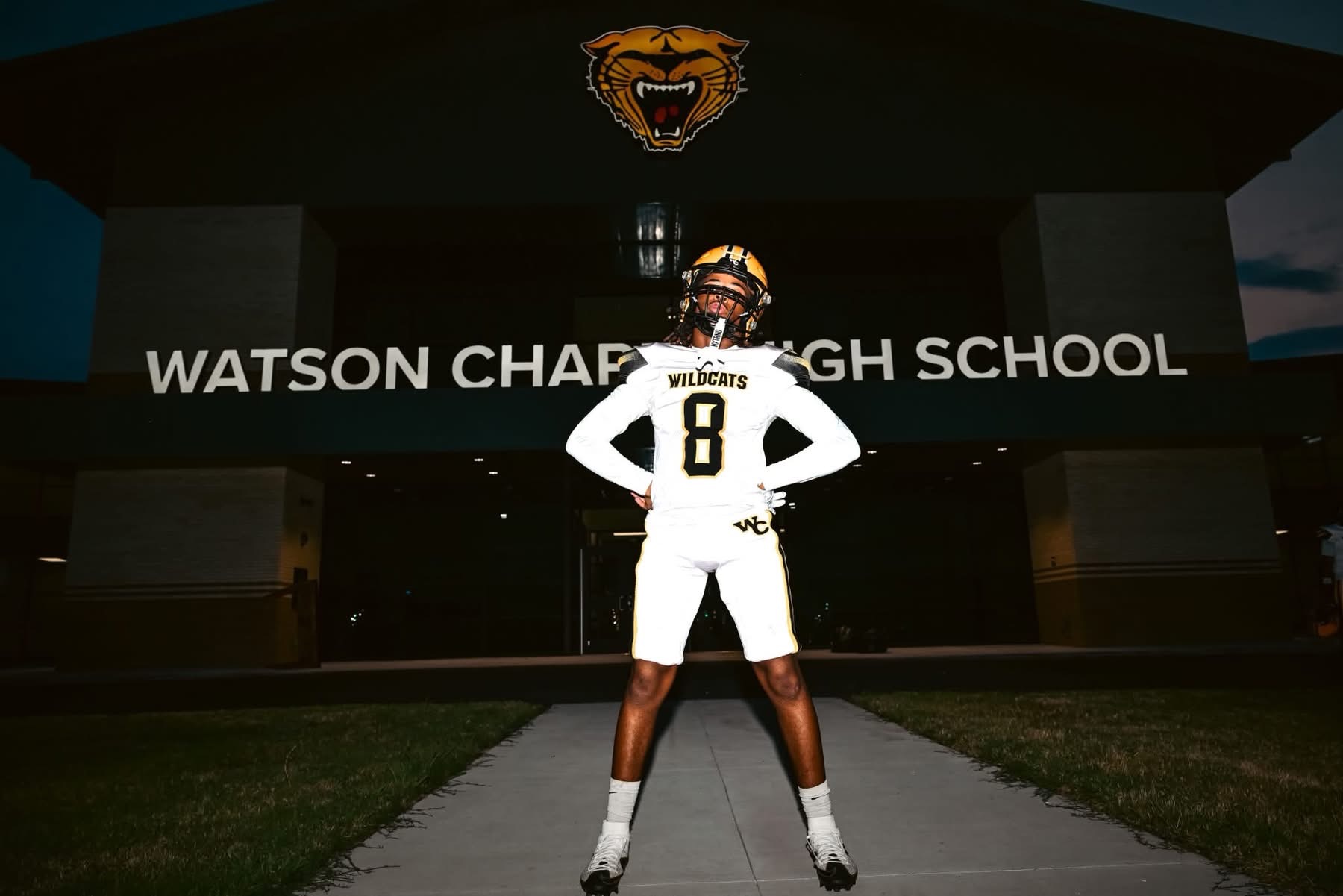 A person wearing a football uniform with number 8 stands in front of a school building.