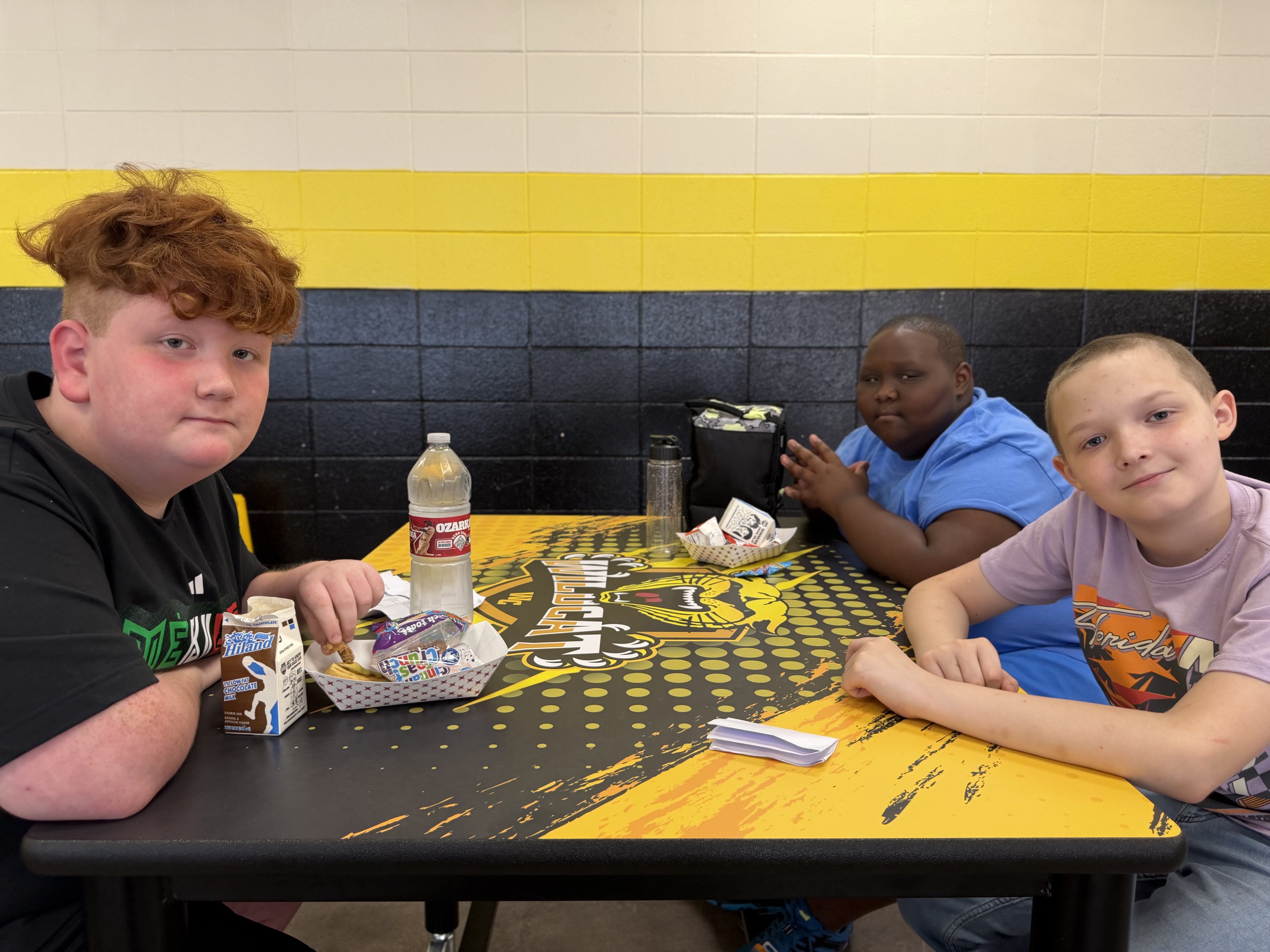 Three individuals seated at a table with a black and yellow surface, a bottle, and various items.