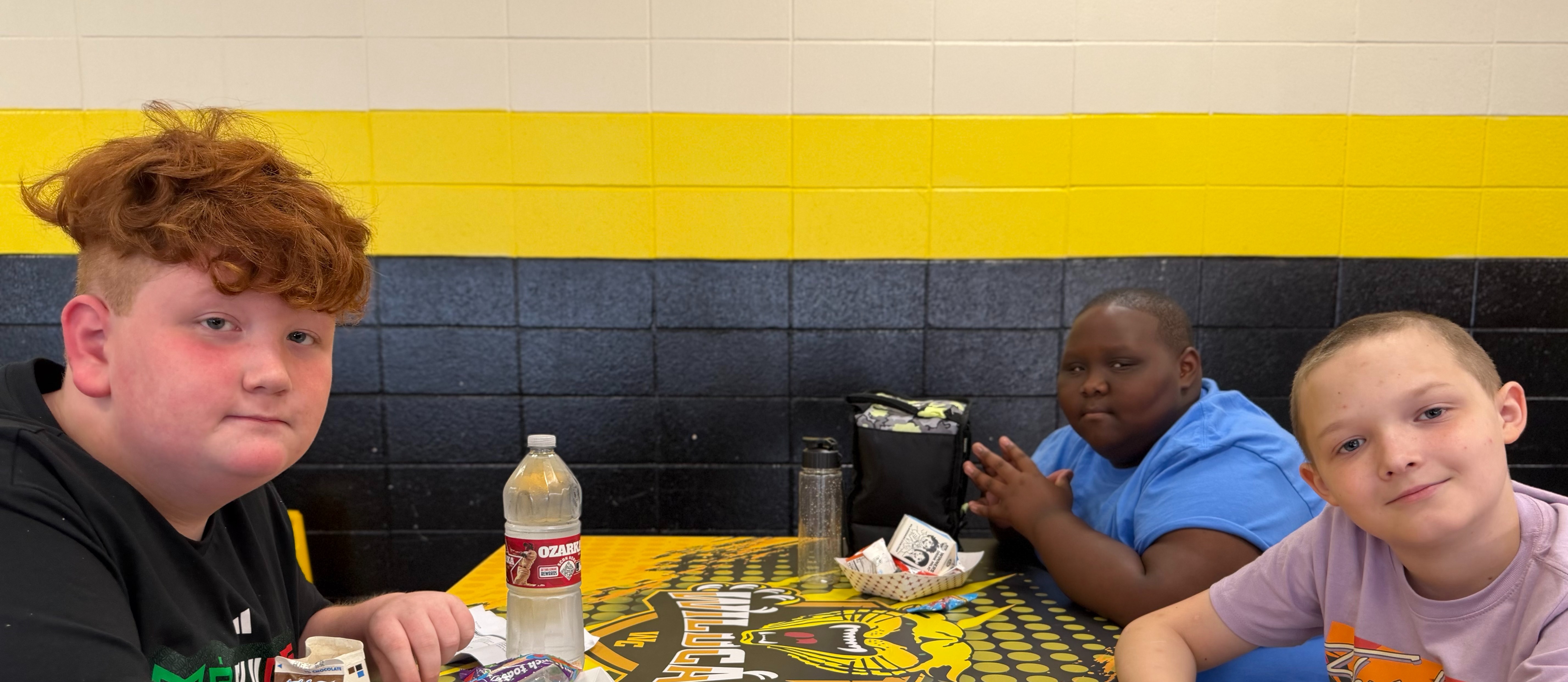 Three individuals seated at a table with a black and yellow surface, a bottle, and various items.