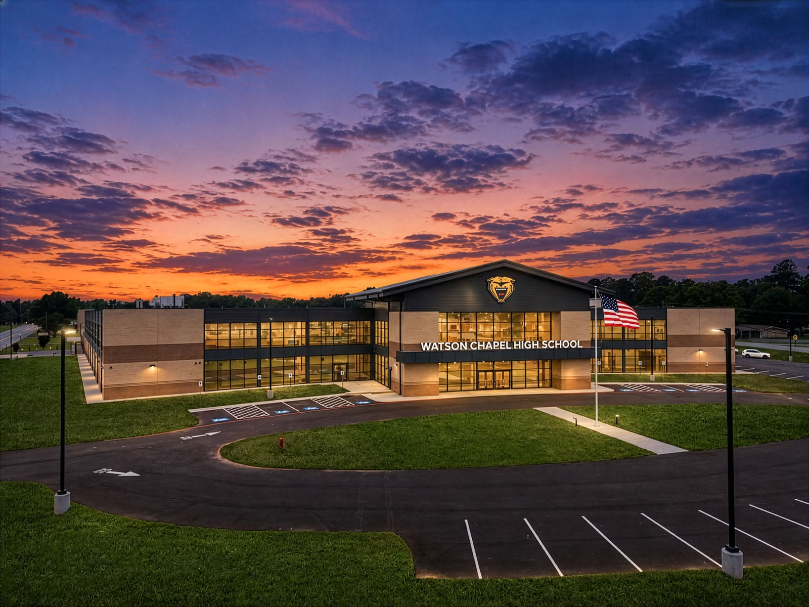Aerial view of a modern building with a flag at sunset. Large windows and a parking lot.