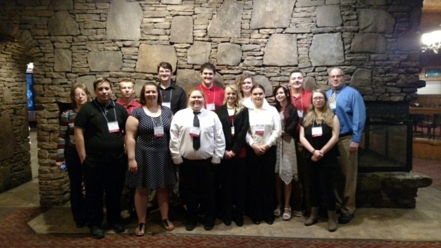 group photo of students and teachers in front of a stone wall