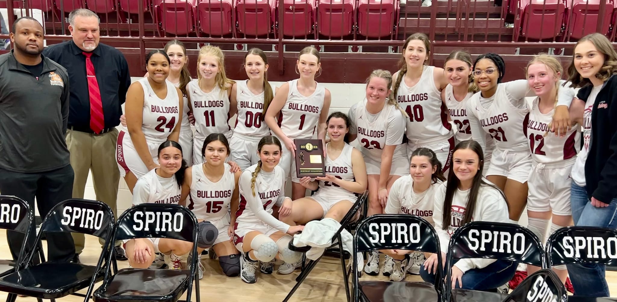 Girl's basketball team poses with trophy in front of bleachers