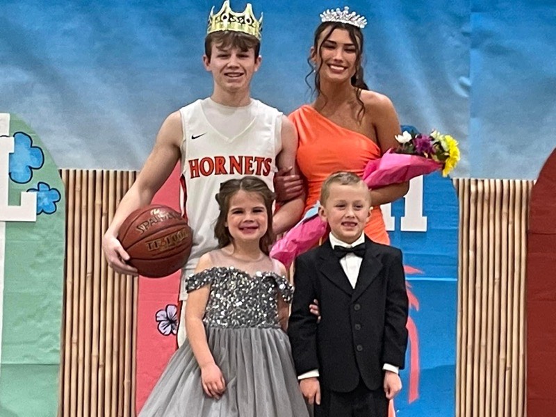 homecoming king and queen in crowns with younger students in front of them - posing for camera 