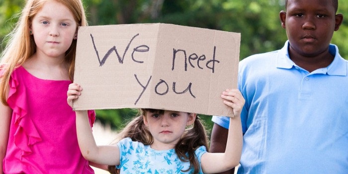 Girl holding a sign that says "We Need You"