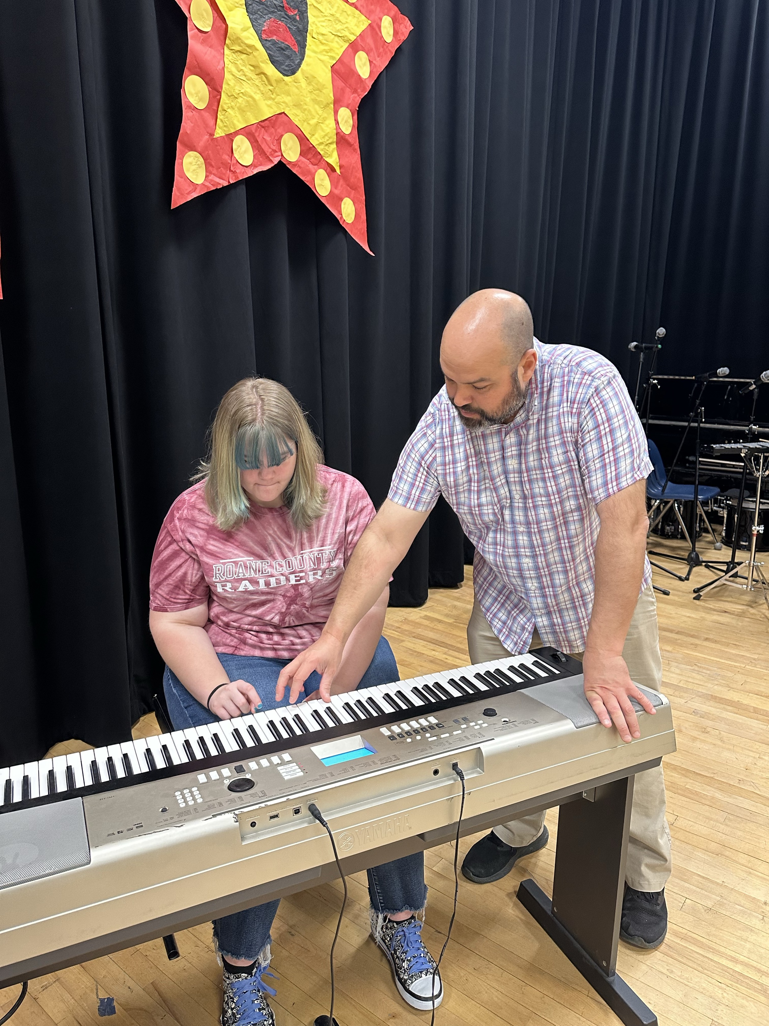 A male instructor assists a female student with using a keyboard instrument.