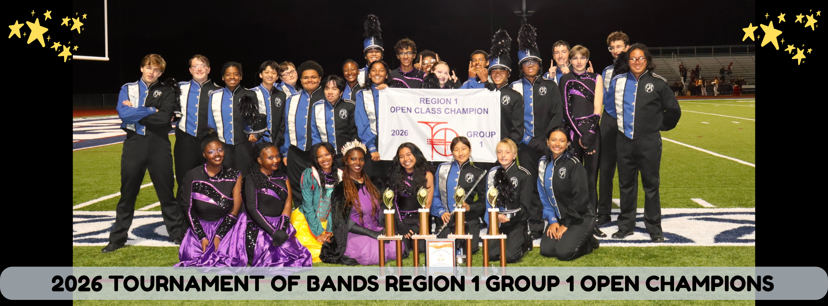 A marching band poses with trophies on a football field at night.