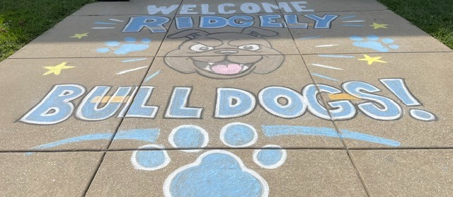 Sidewalk with "Welcome Ridgeley" and "Bull Dogs!" written in blue chalk. Paw prints and stars are drawn.