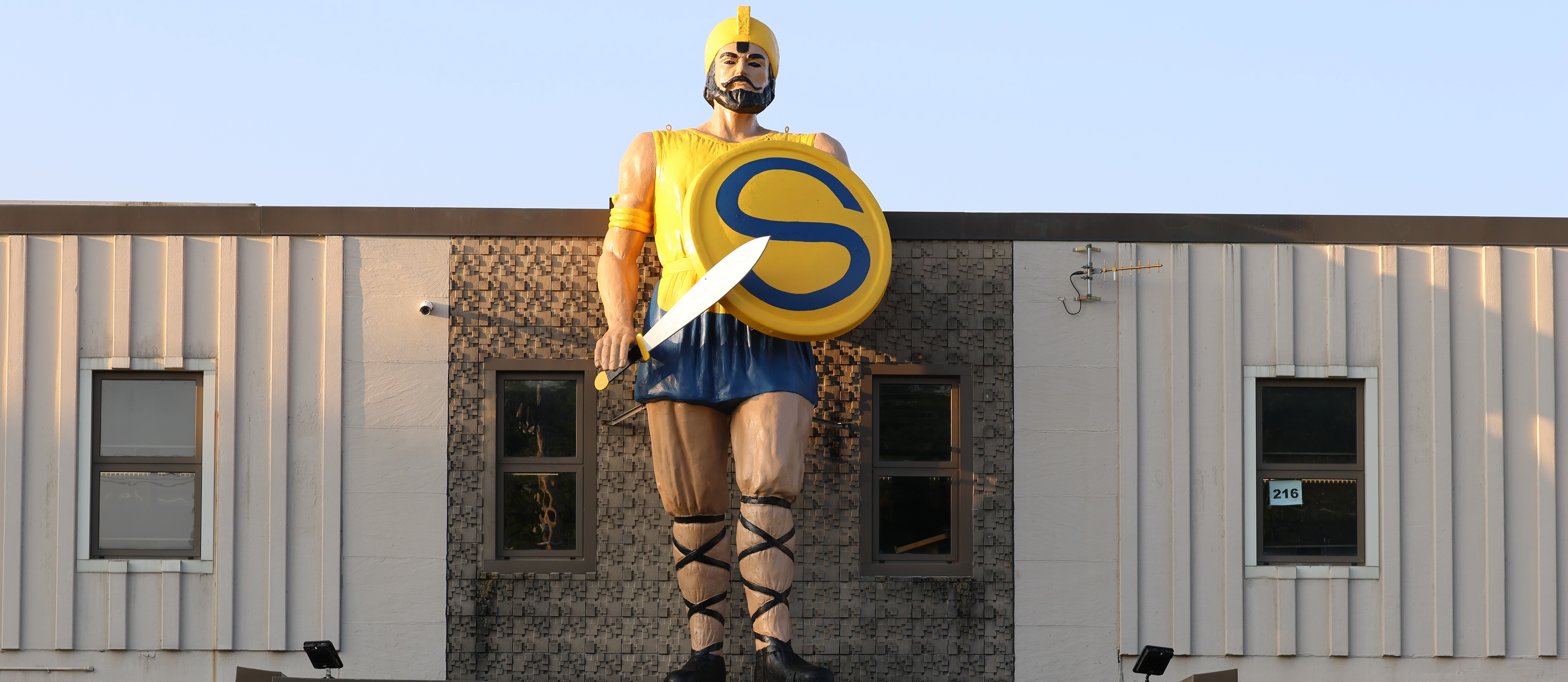Large figure of a warrior with a shield and sword on top of a building.