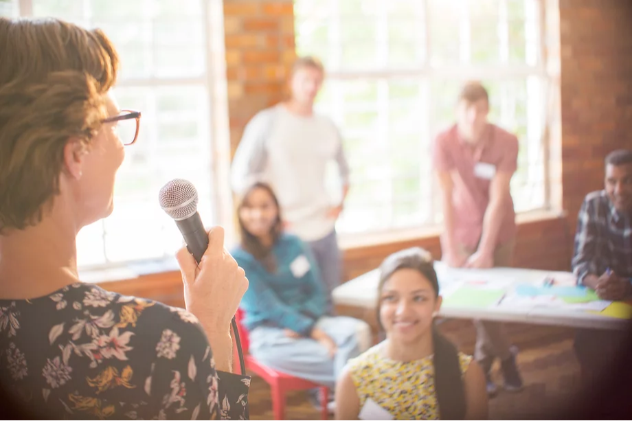 Woman speaking with a microphone to a small crowd