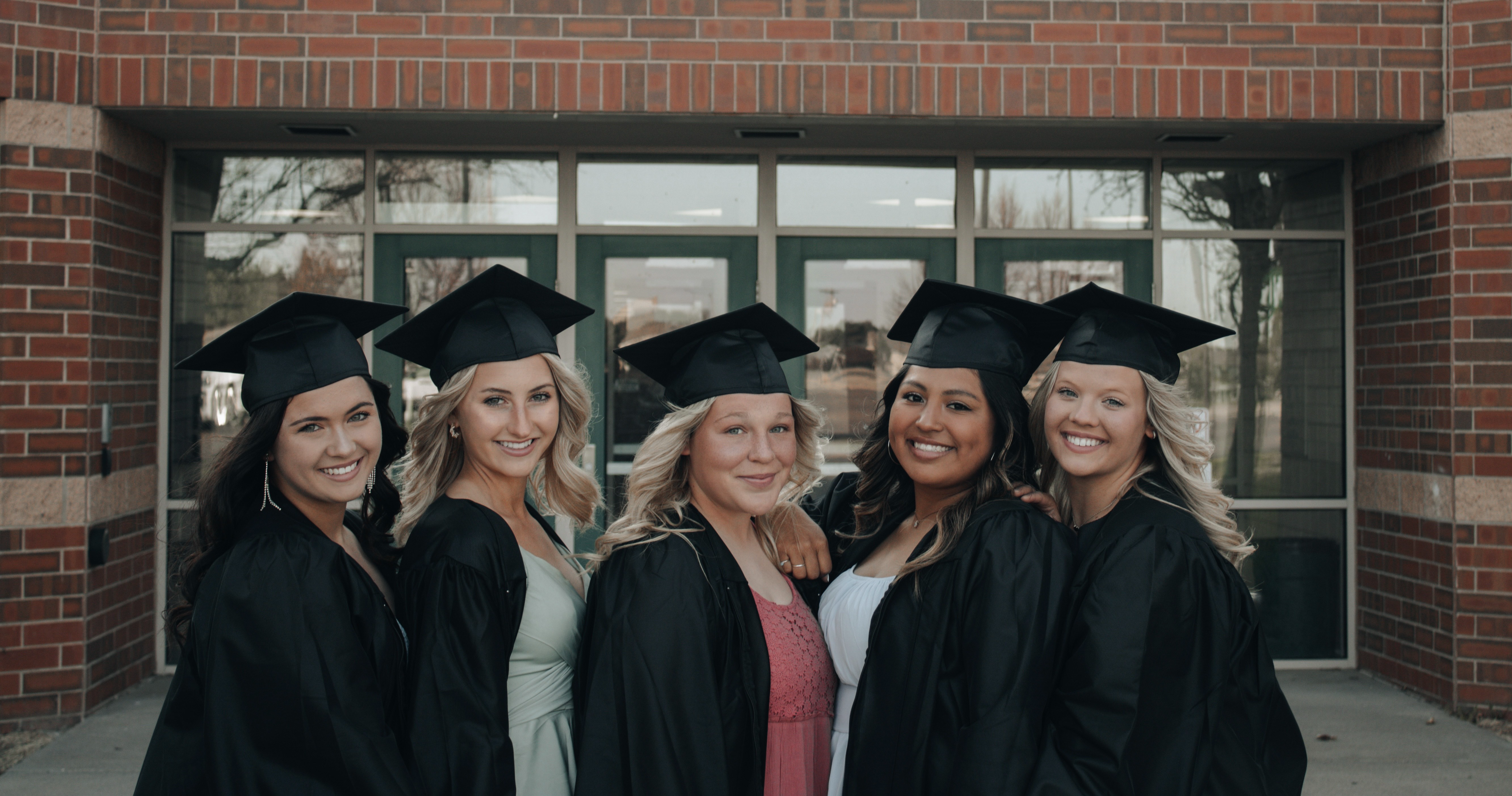 Graduating High School girls standing in front of school in caps and gowns.