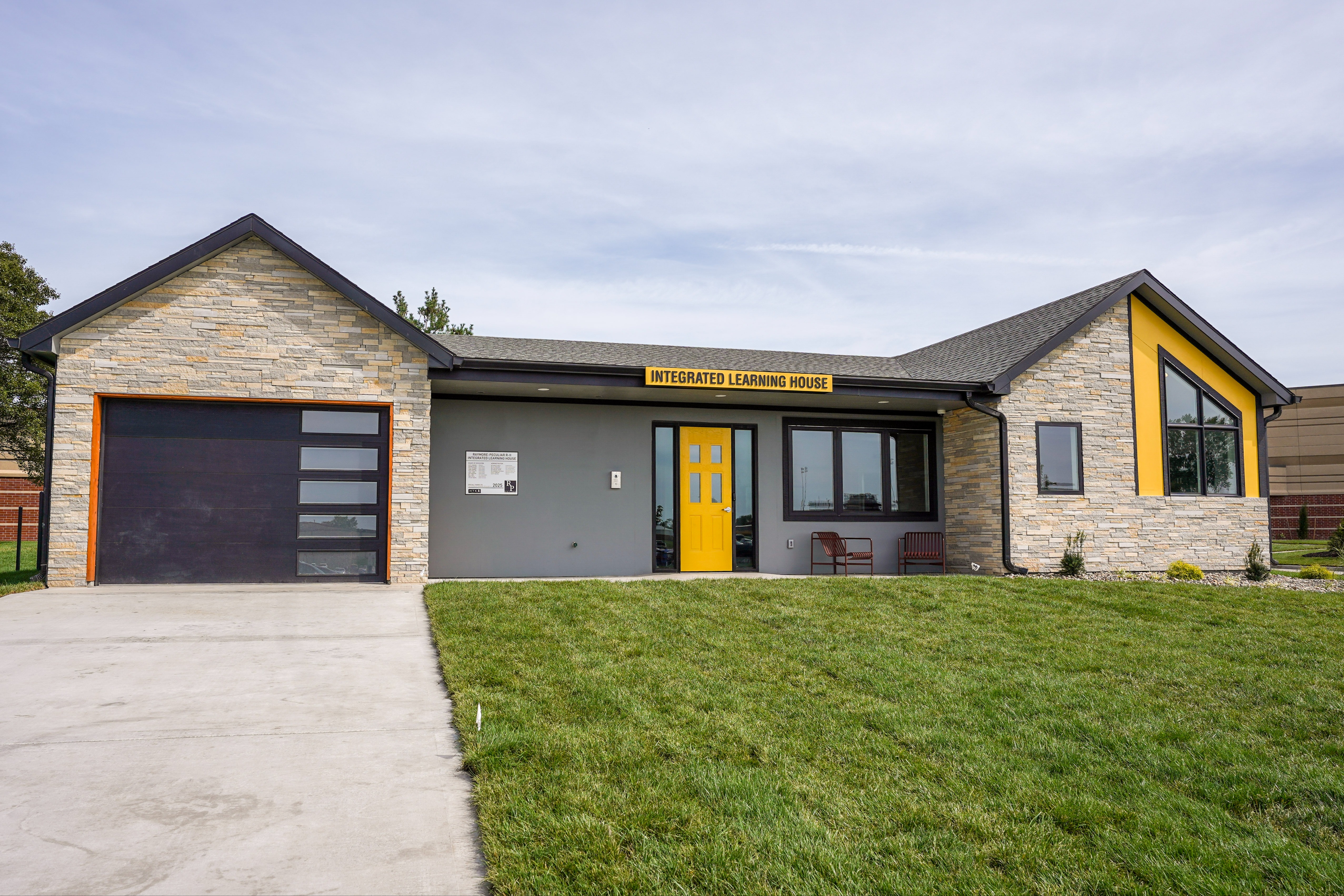 The front of a house with limestone brick and a yellow front door. A sign above the front door reads, "Integrated Learning House"