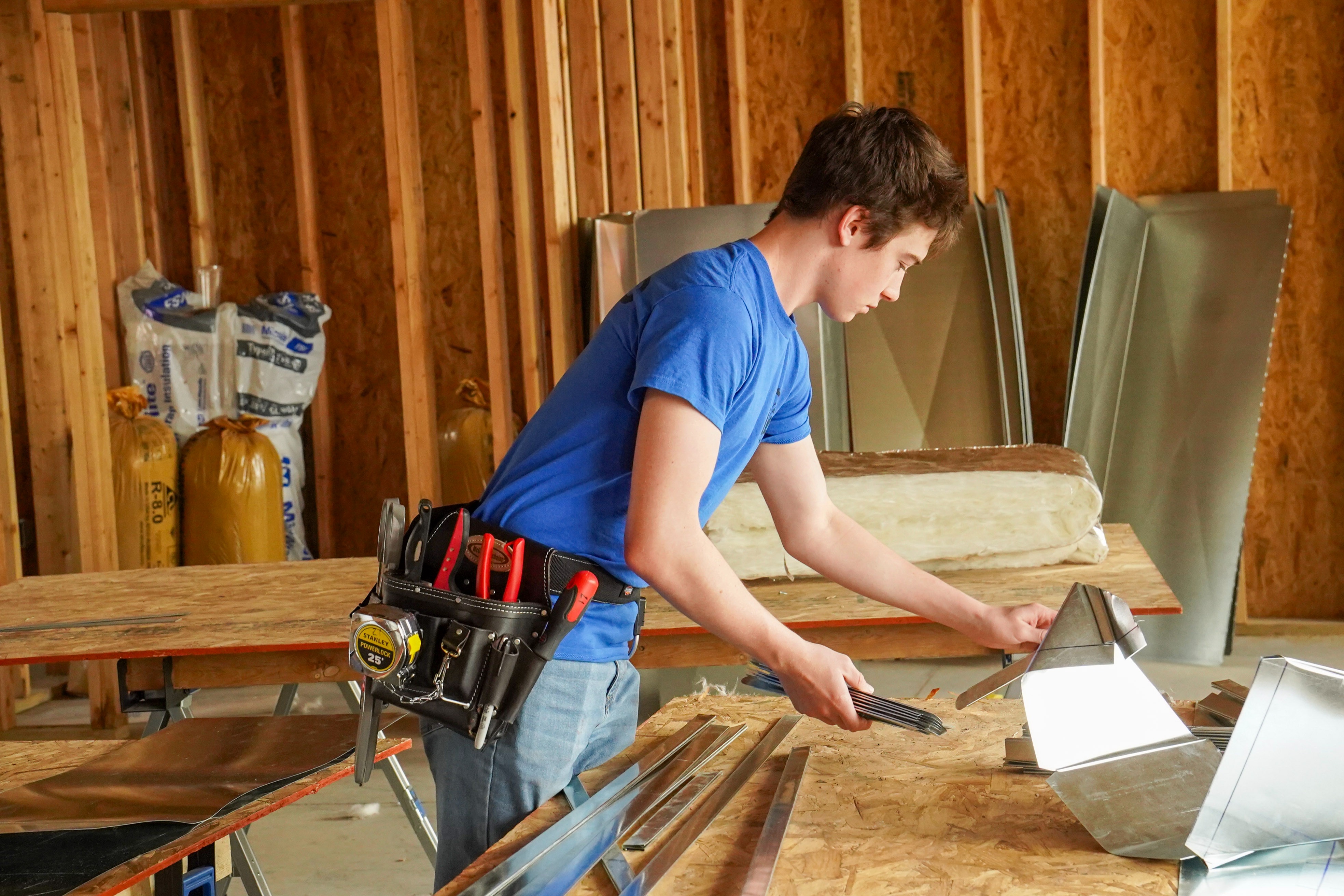 A young man with a tool belt on work at a work bench in a construction site.