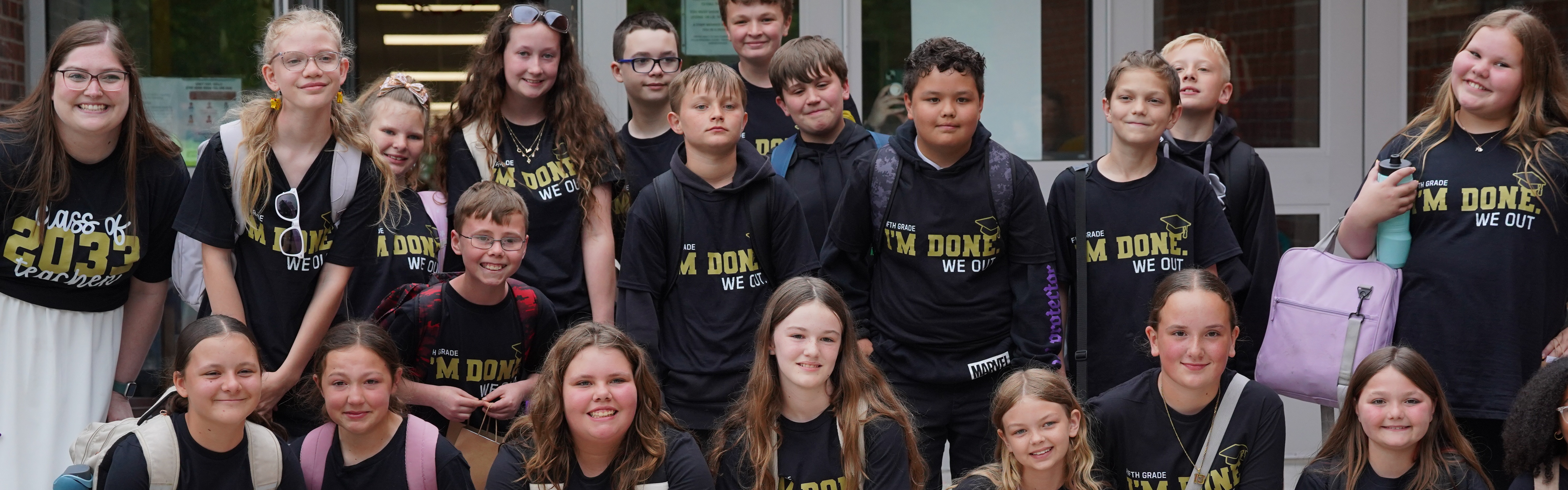 A group of students with black and gold shirts on stand together with some crouching in front.