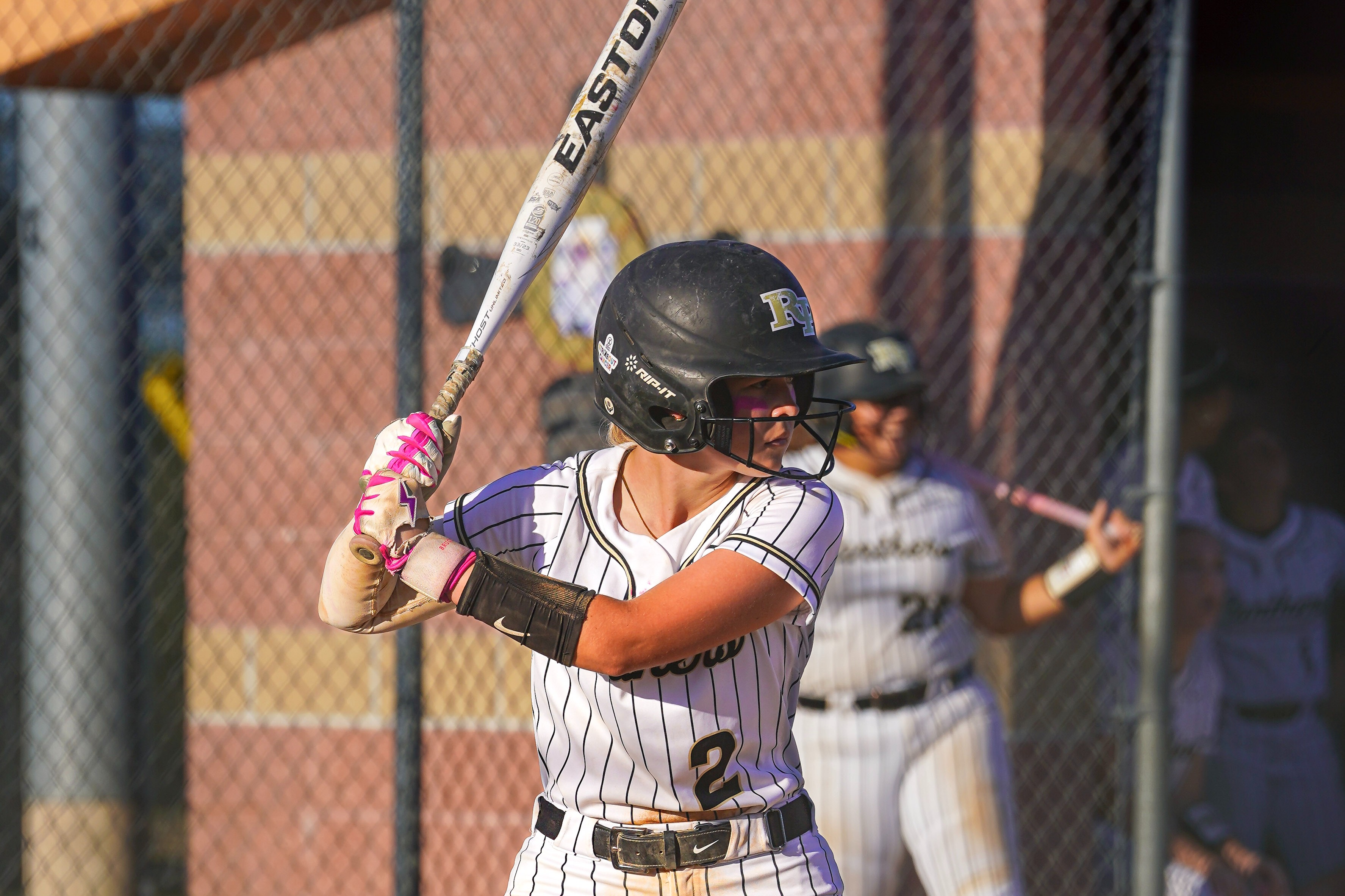 A softball player in a striped white uniform stands in a batting stance.
