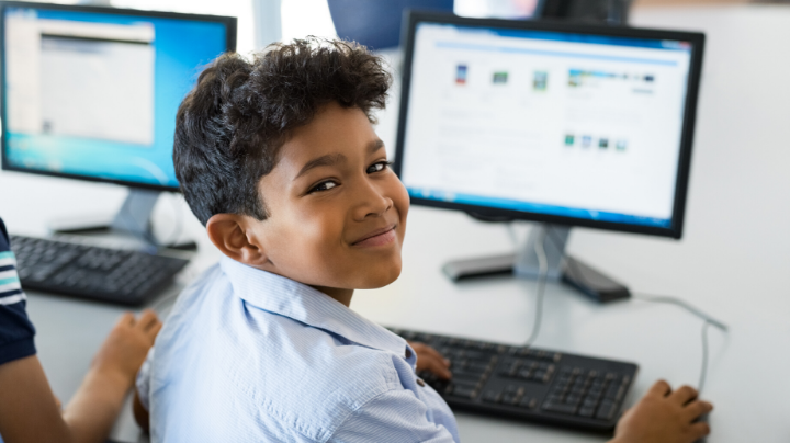 A young student smiling over his shoulder from a computer