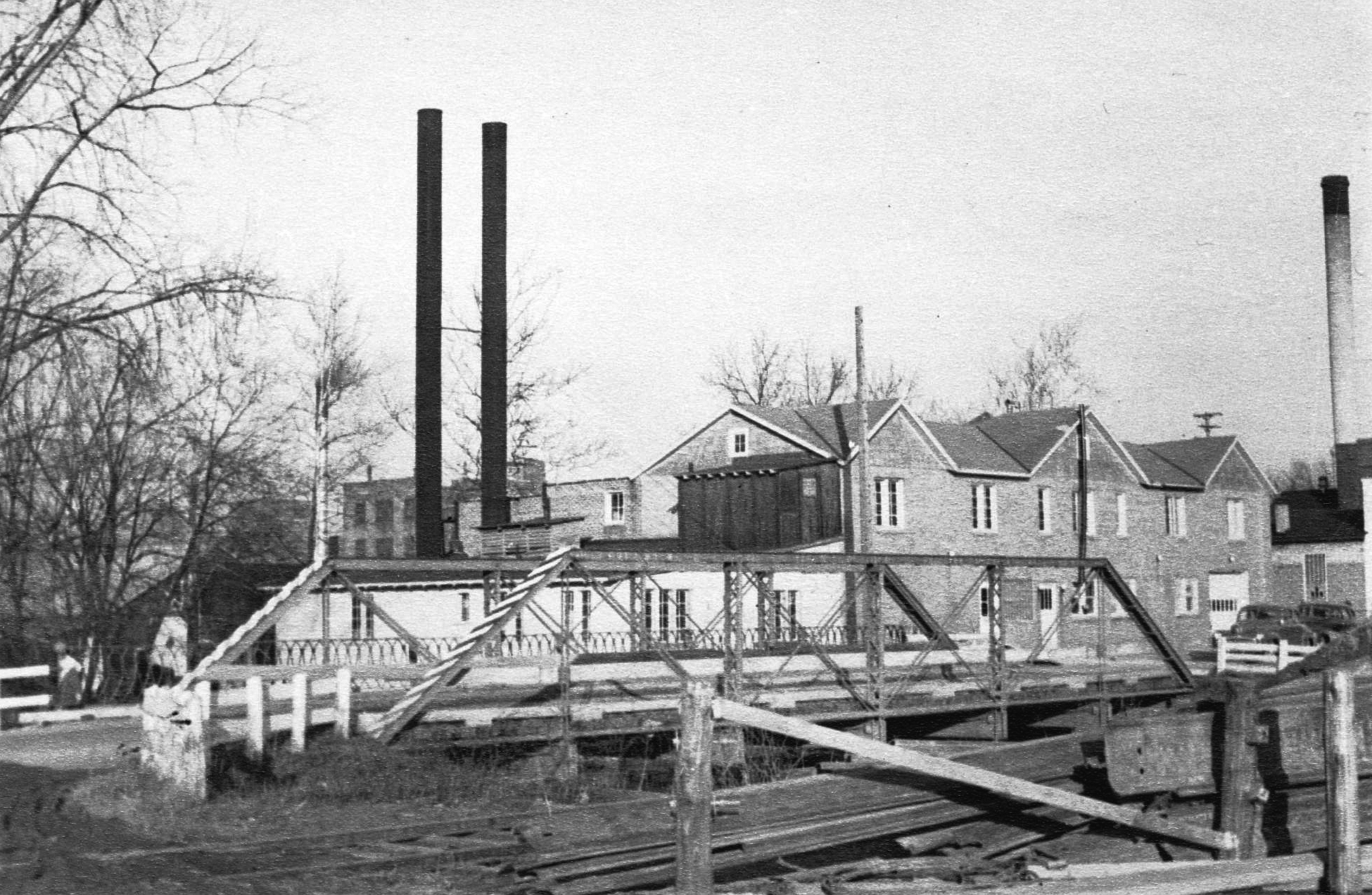 Old steel-frame bridge on W. Main Street over Bean Creek, looking northeast to Anderson’s Creamery.  Replaced Nov. 1949.