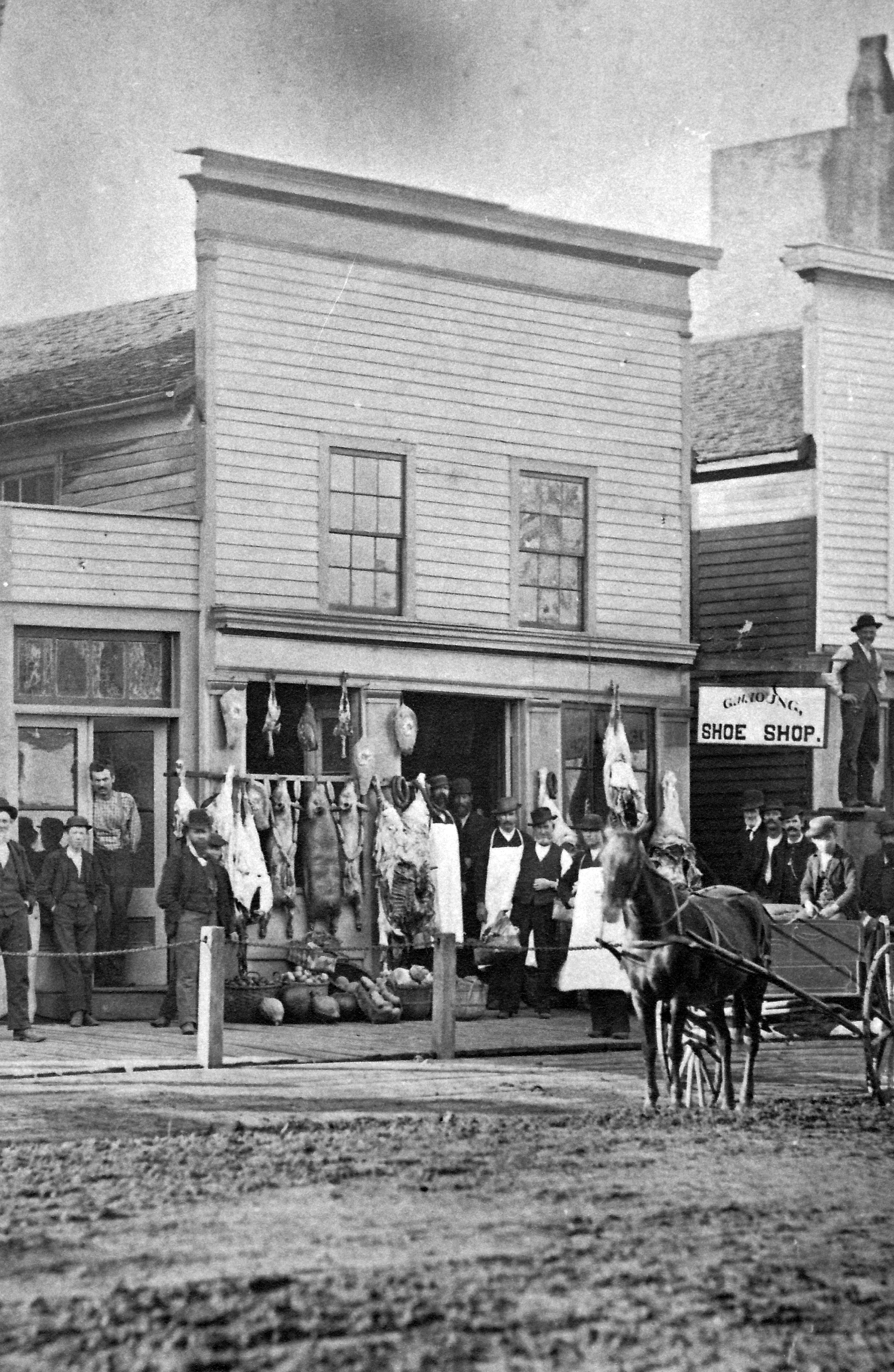 Original meat market that stood on site of Knoblauch’s Market, built by Alfred Whitman April 14, 1856.  This picture taken in 1882 show Andrew Stephenson (donor of South or Stephenson Park), Val Houseman, Charles Chase, Marve Davison, Unknown, William Murfitt (father of Carrie and Ida Murfitt), and Samuel McFarlane, the owners and operators of the market, Elva Plummer, Spencer T. Snow, proprietor of the Morenci Exchange Hotel, Frank Reader, Horatio Wilson, an early settler, Duane Downer, Unknown, Unknown, Freeman Smalley (on the scaffold), Charles McFarlane (in the delivery wagon).